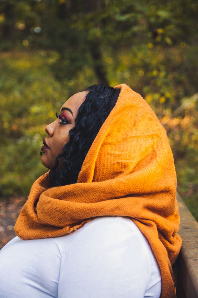 Young Black woman wearing an orange knit head wrap sitting outdoors in an autumn forest.