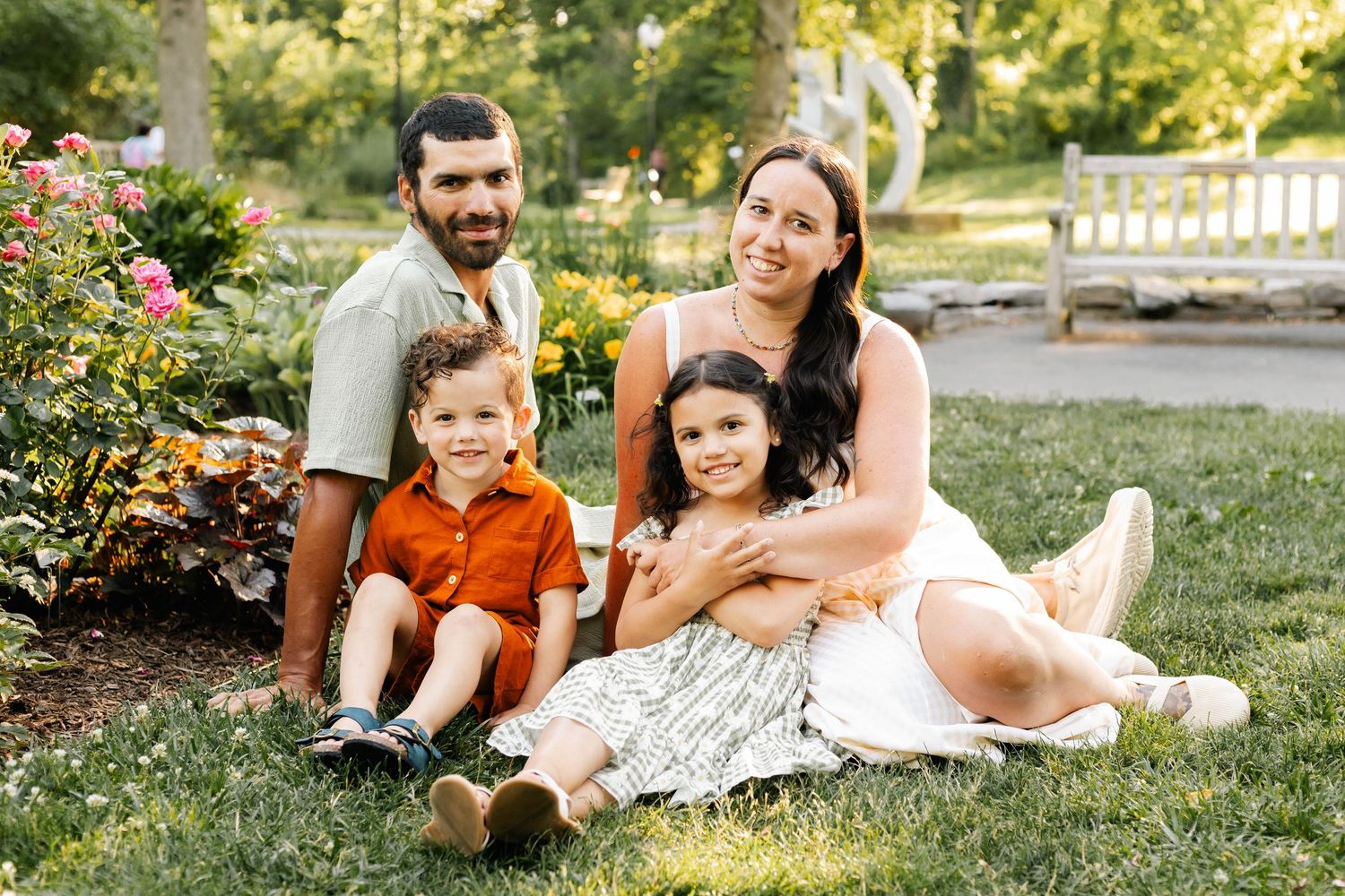 Happy family of four sitting on grass near colorful garden flowers on a sunny summer day at Reading Museum Arboretum.