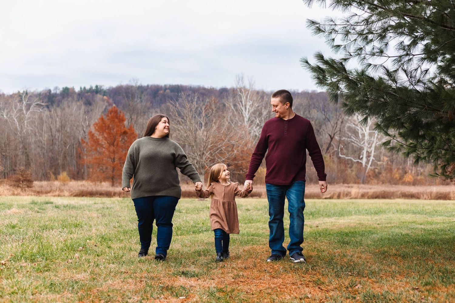 Family of three walks hand-in-hand through an open field on a cloudy autumn day in nature in Pottstown, PA.