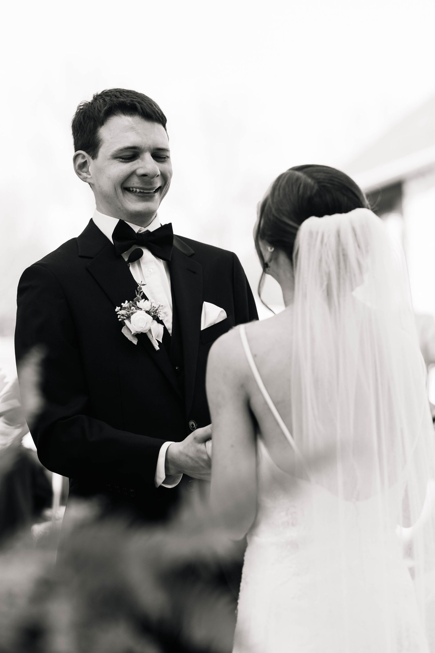 Black and white photo of smiling groom holding brides hands during outdoor wedding ceremony exchange.