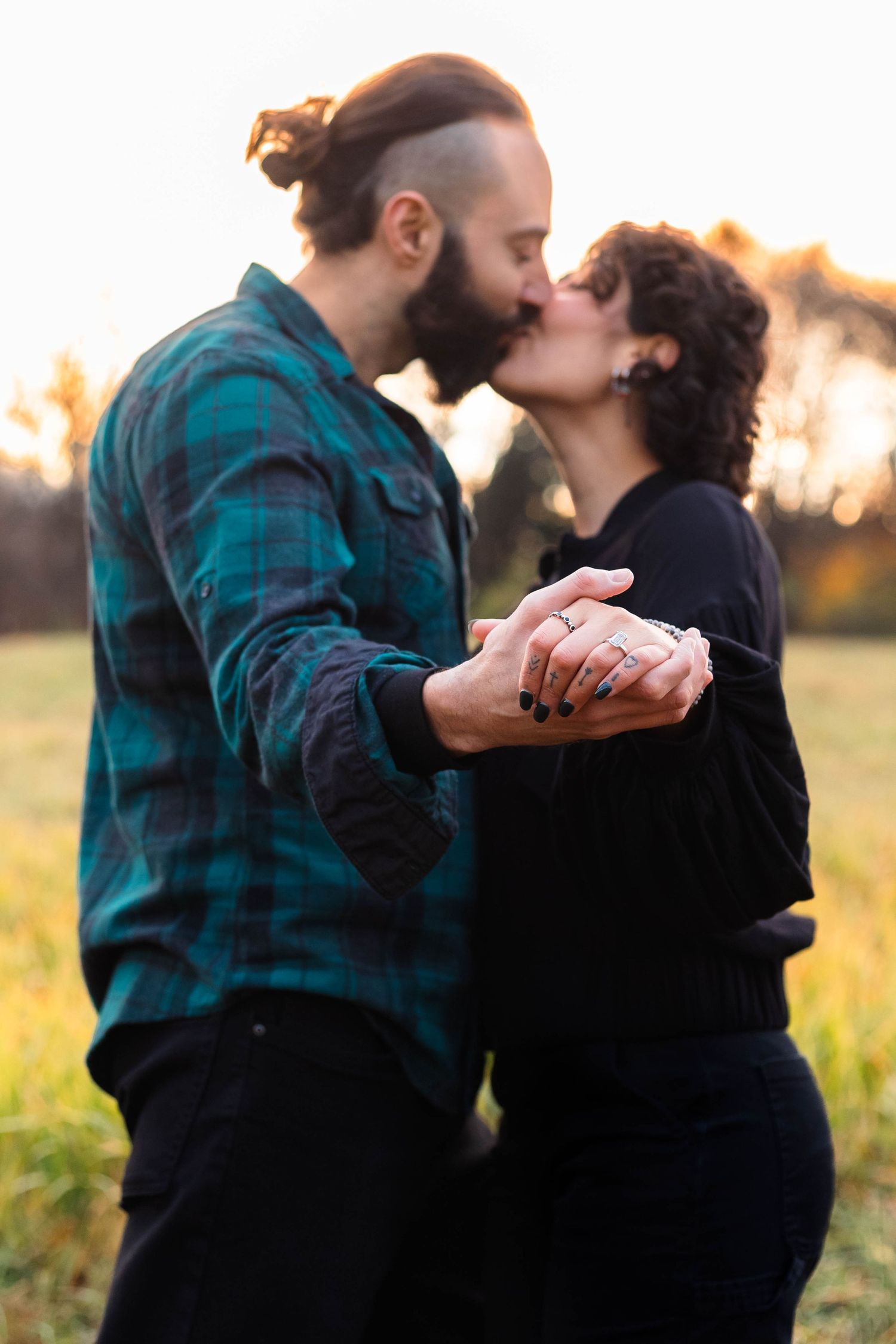 Couple kissing at sunset in a fall meadow while holding hands showing engagement ring in West Chester, PA.