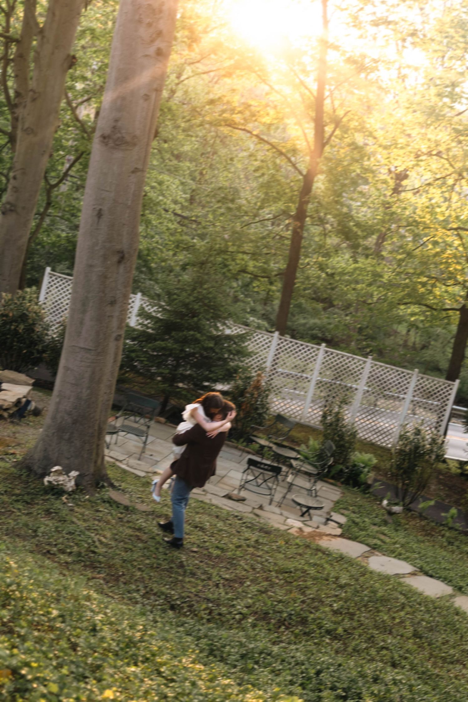 Couple embracing and spinning joyfully in a sunlit garden with lush green trees in West Chester, PA.