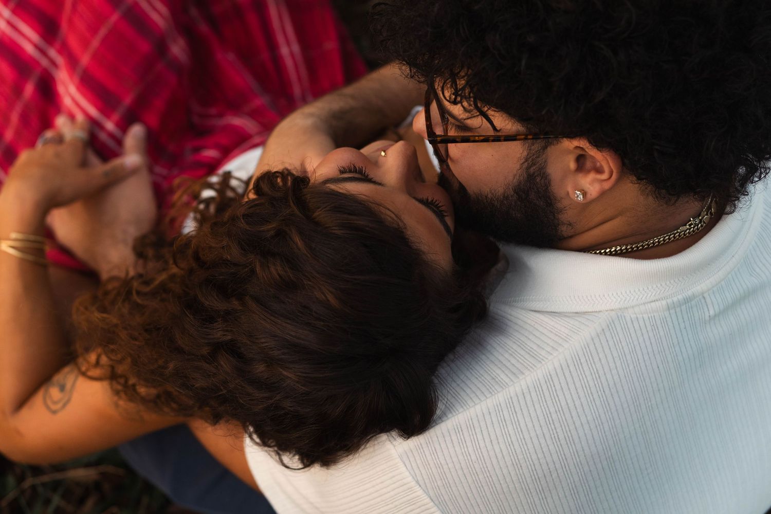 Overhead close-up of a tattooed couple sharing a tender kiss while lying in the grass in Elverson, PA.