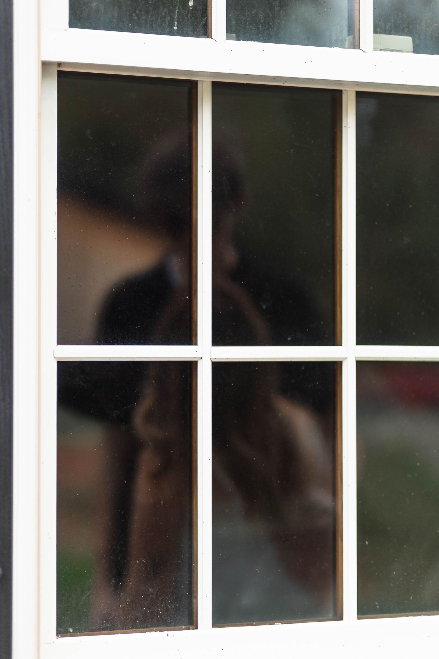 A blurred silhouette of a couple sharing an intimate moment seen through a white-framed window during an engagement session in Oley, PA.