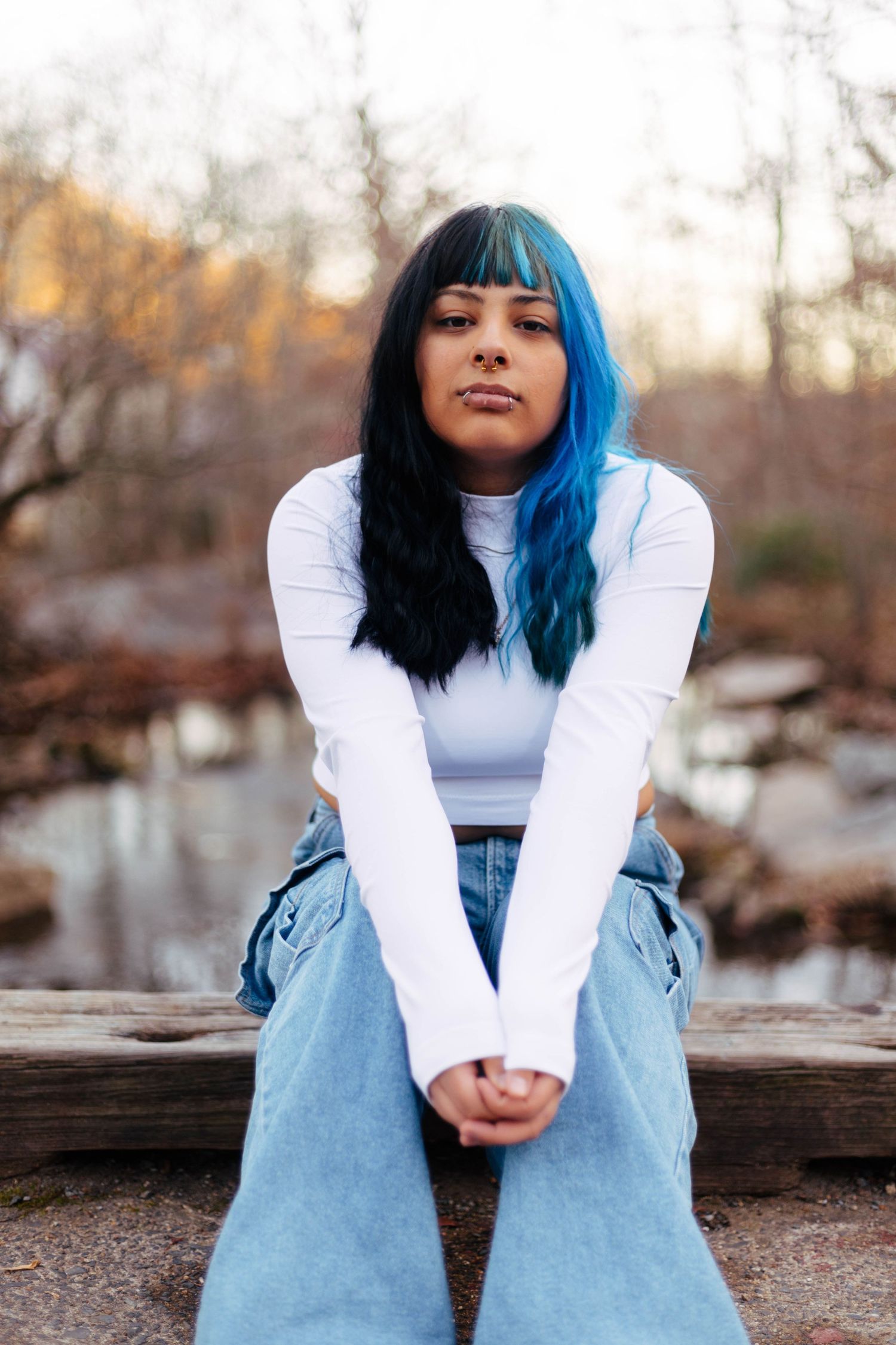 Pottstown senior with blue and black split-dyed hair sitting outdoors in white top and wide-leg jeans.