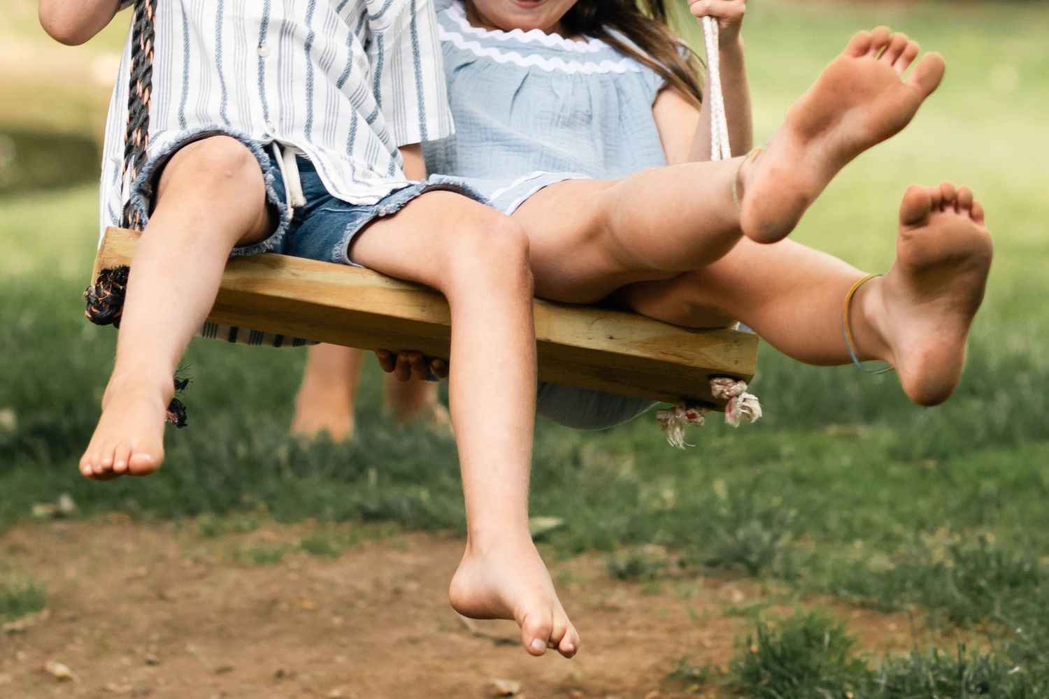 Two barefoot children sitting together on a wooden swing outdoors on a sunny day in Boyertown, PA.