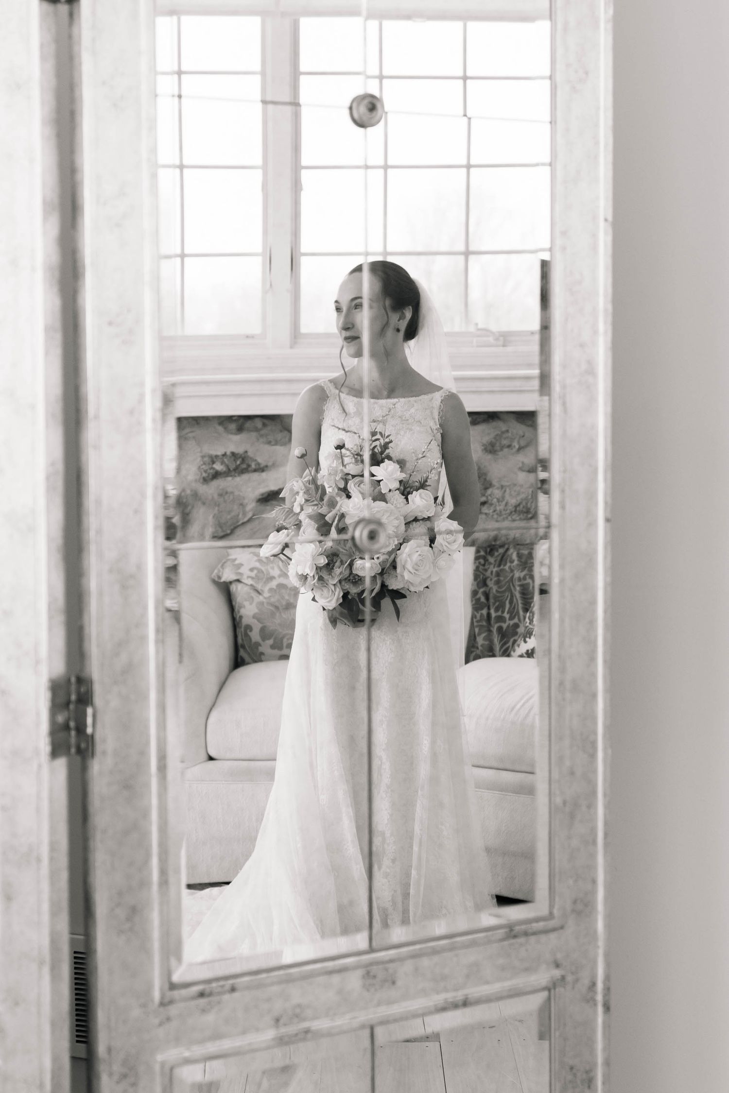 Elegant black and white mirror reflection of bride in white gown holding floral bouquet near window.