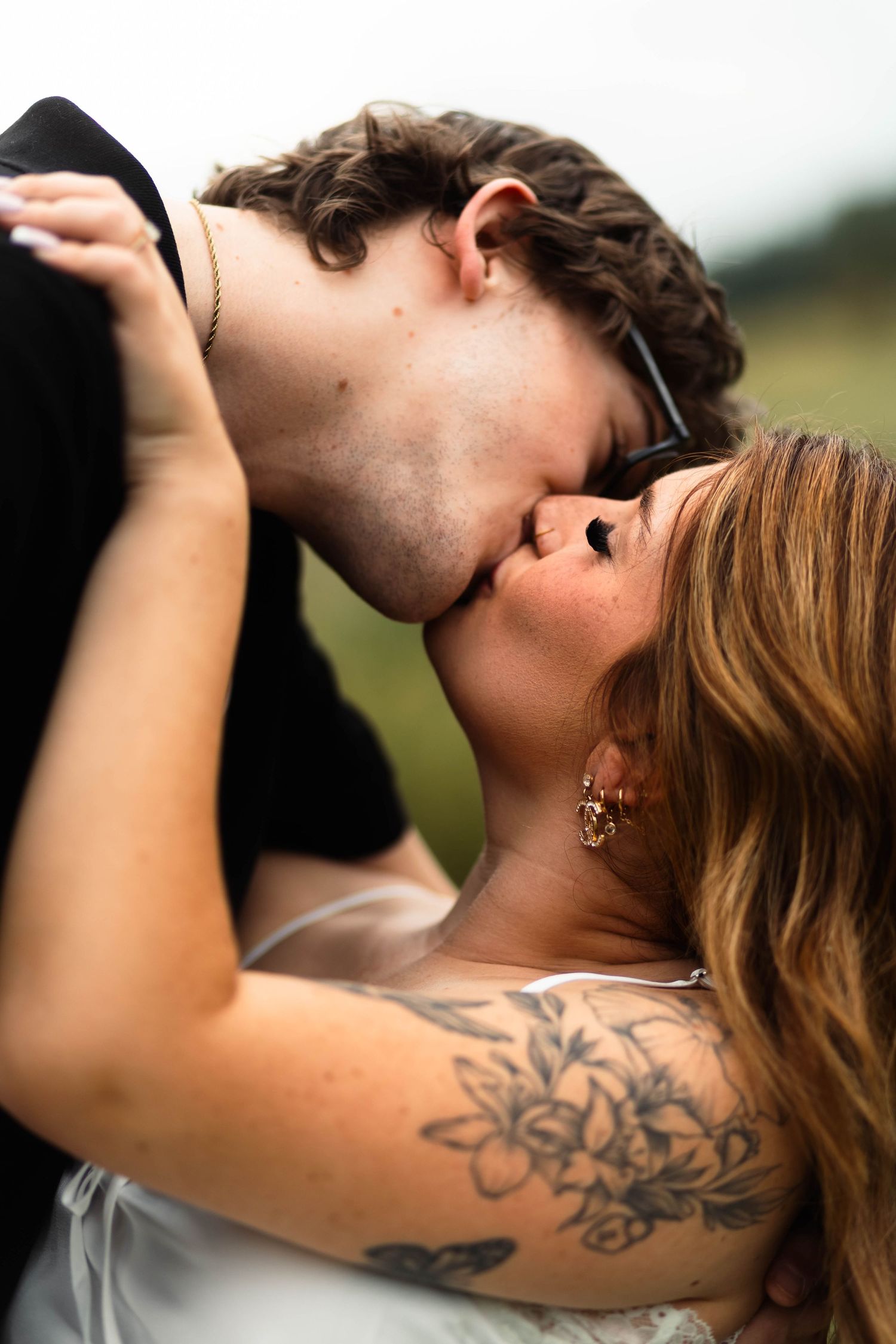 A couple shares a passionate kiss outdoors, woman with floral shoulder tattoo in white dress, man in black shirt in Oley, PA.