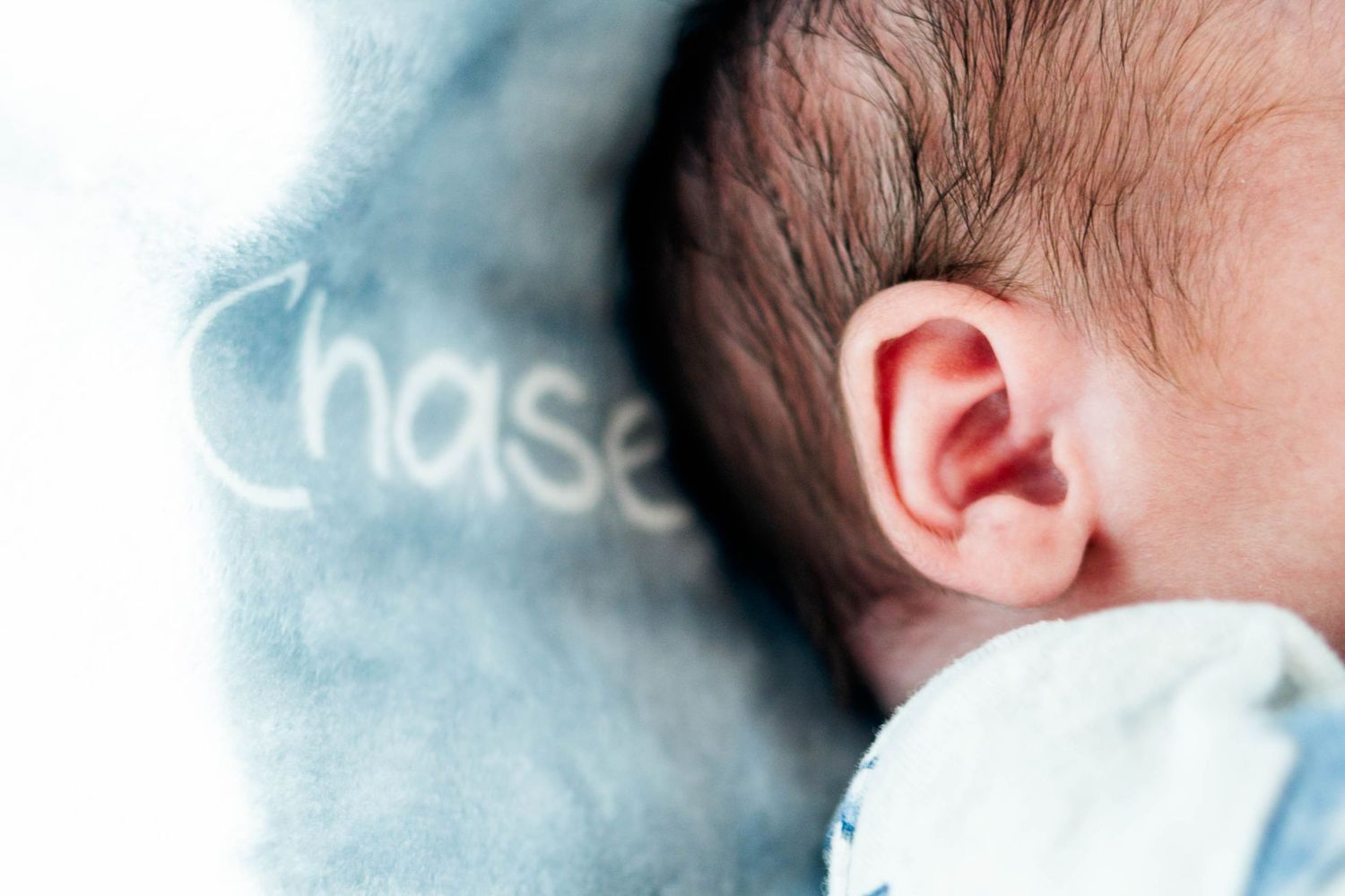Close-up of newborn baby's ear resting on a soft blue blanket embroidered with the name Chase in Philadelphia, PA.