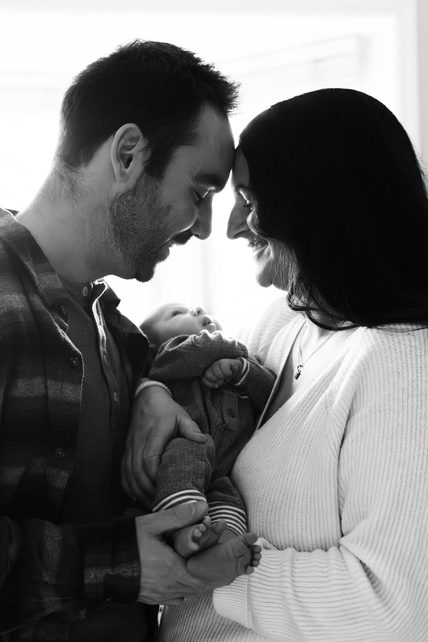 Black and white portrait of new parents touching foreheads while holding their newborn baby in Pottstown, PA.