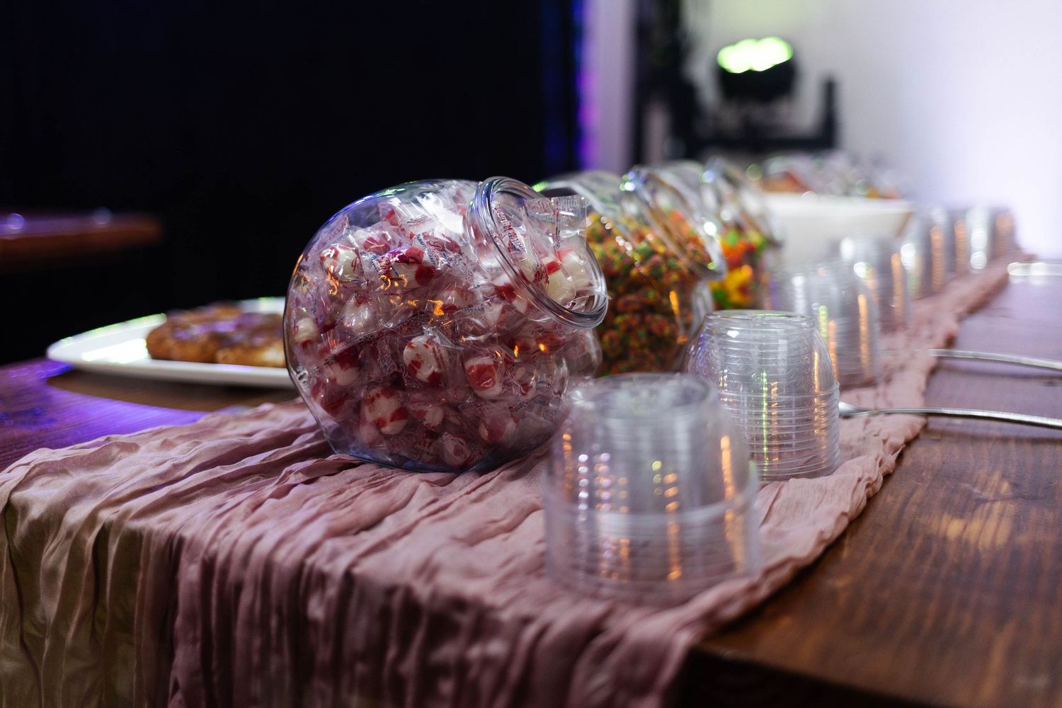Elegant candy bar table with glass jars filled with colorful sweets and plastic cups at a wedding in Pottstown, PA.