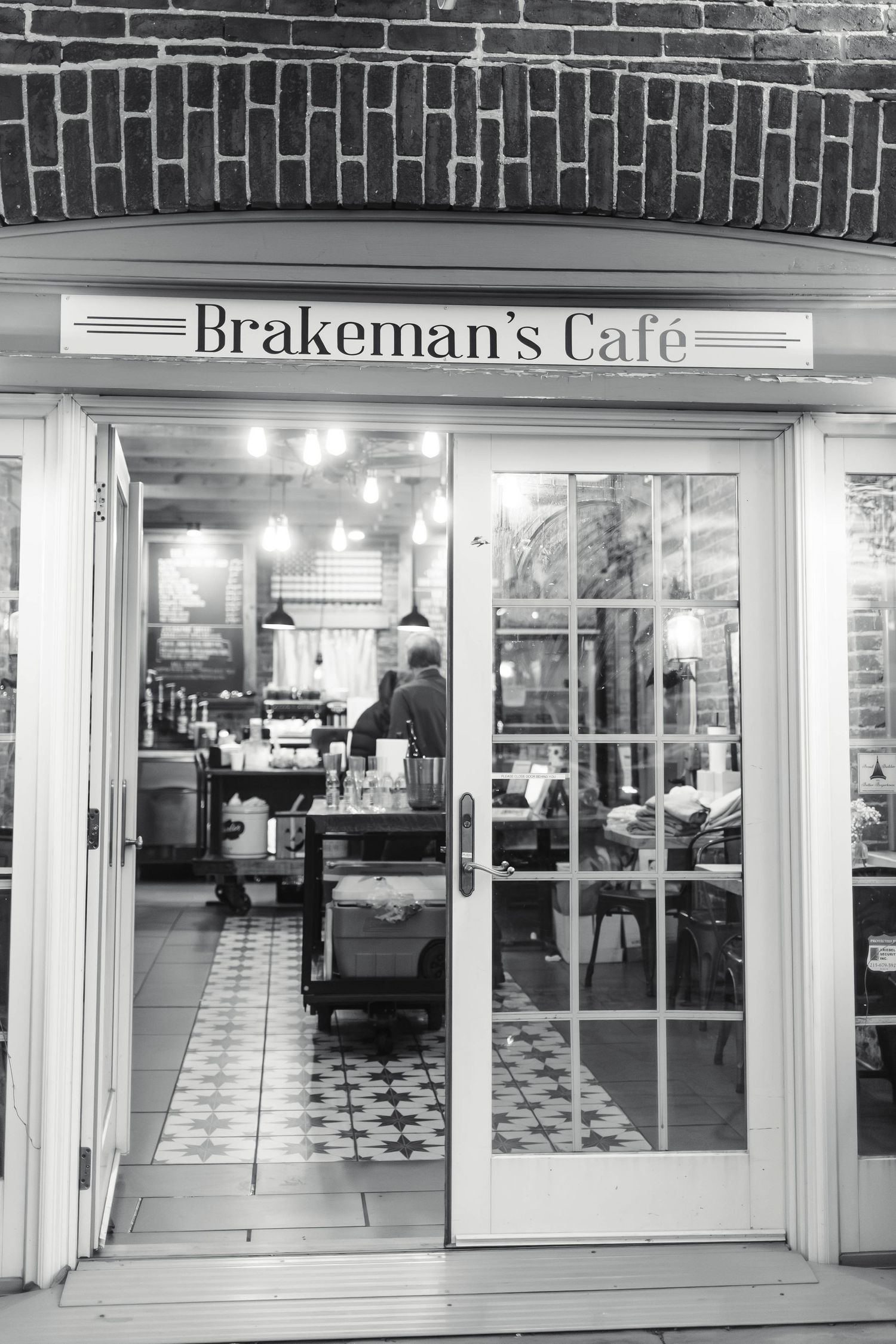 Black and white exterior photo of Brakemans Cafe entrance with open glass doors and interior lighting.