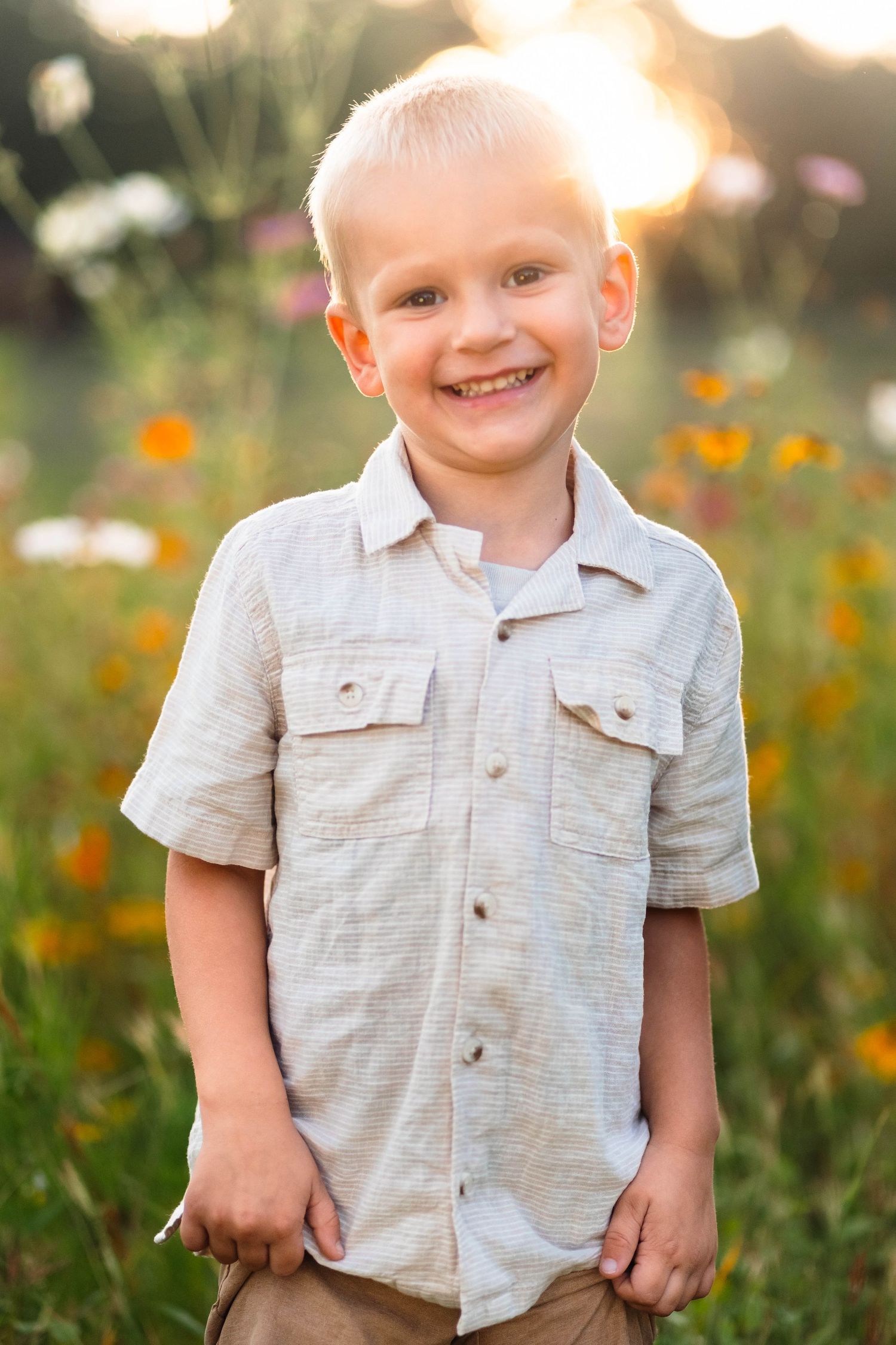 Happy blonde boy in a beige shirt smiling in a colorful wildflower field at sunset in Pekriomenville, PA.