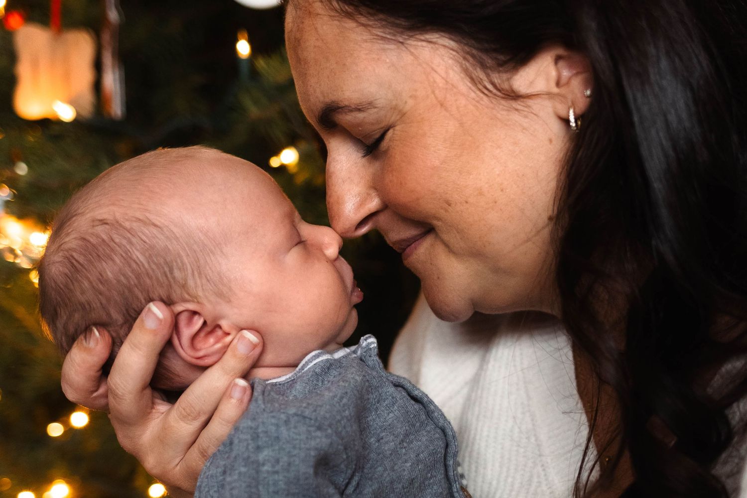 A loving mother tenderly touching foreheads with her newborn baby near Christmas lights during an at home newborn session in Pottstown, PA.