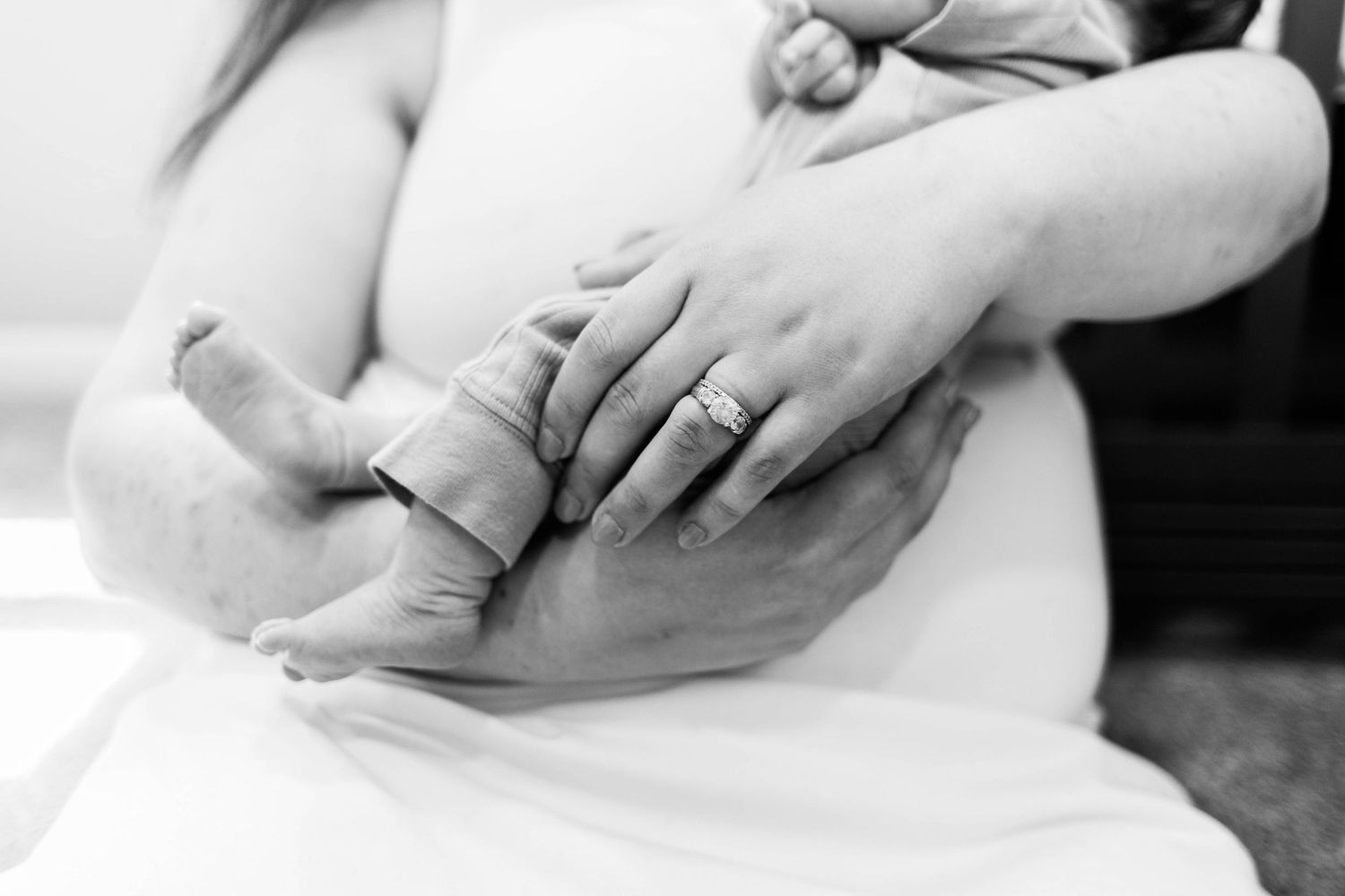 Black and white close-up of newborn baby hand held by mother wearing diamond engagement ring during an at home newborn session Philadelphia,