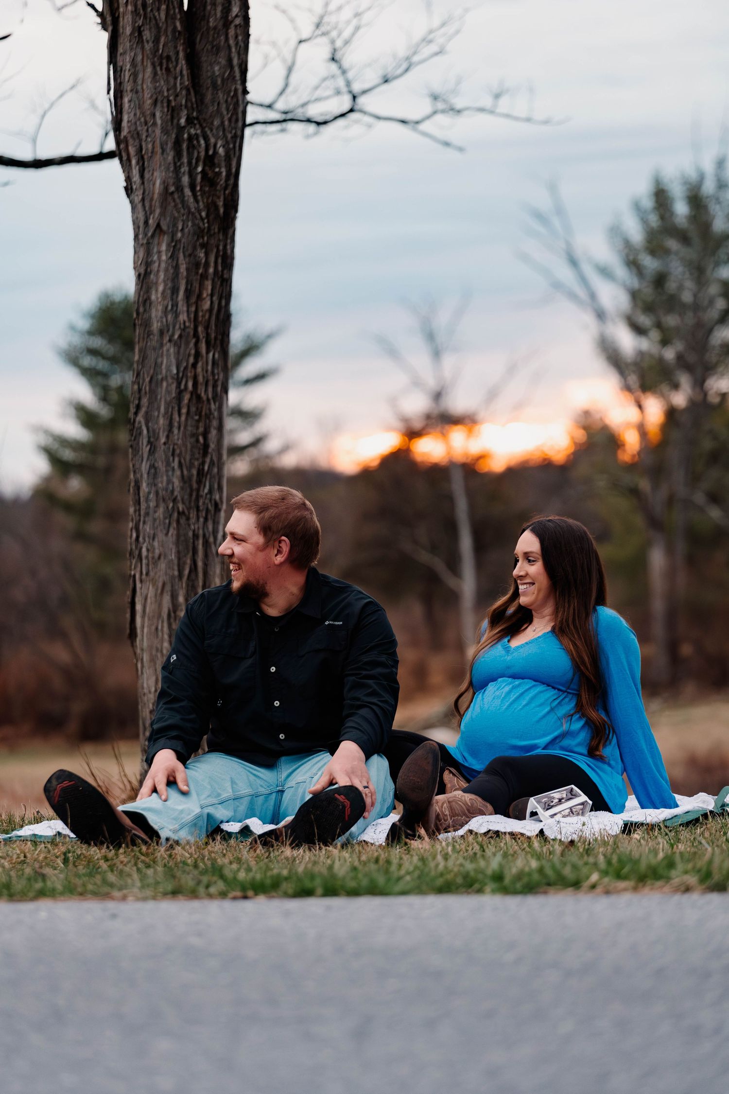 Expecting couple sitting on blanket under tree at sunset during outdoor maternity photography session at Daniel Boone Homestead.