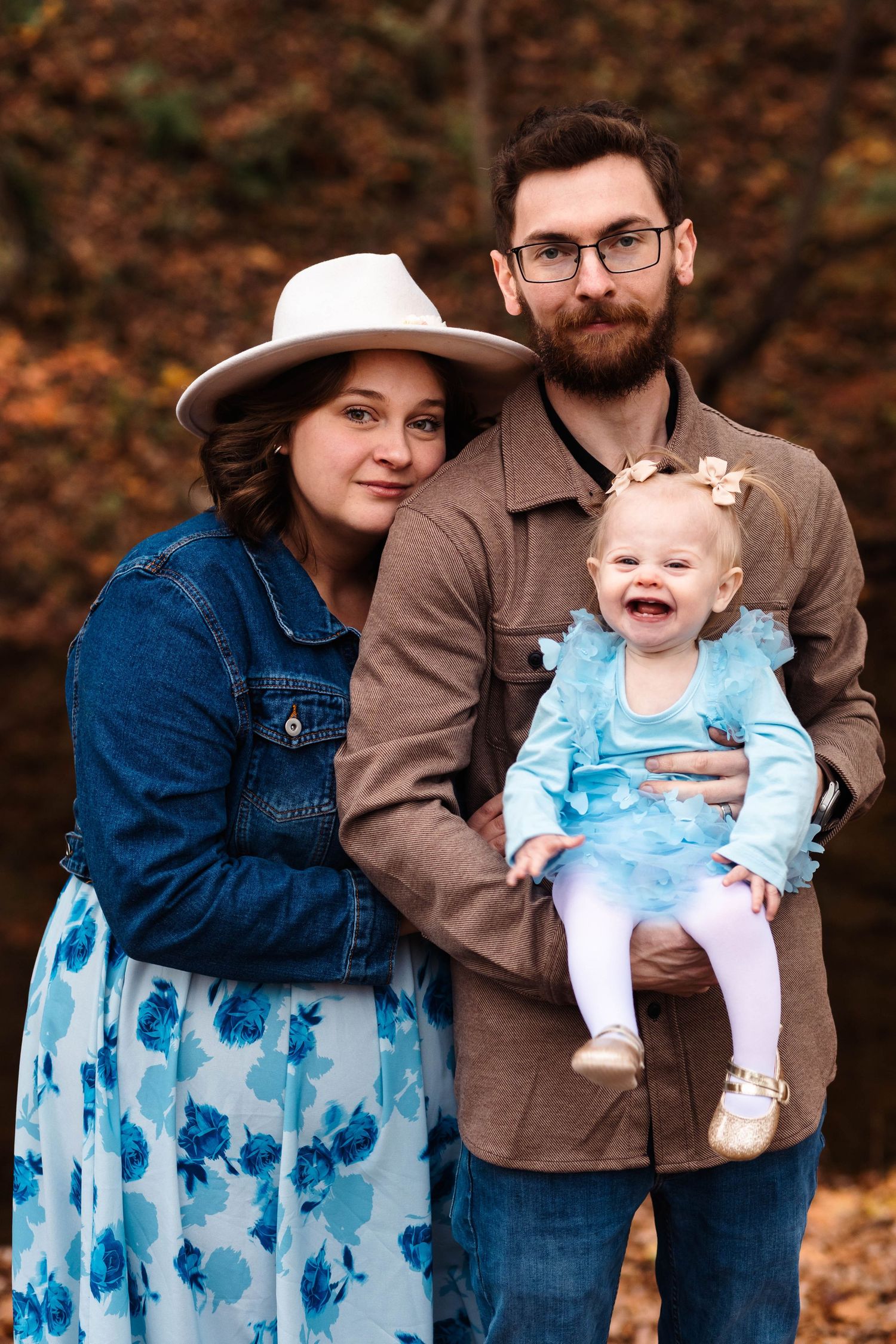 Family portrait with bearded dad, mom in floral dress and white hat, holding laughing baby in blue tutu in Boyertown, PA.