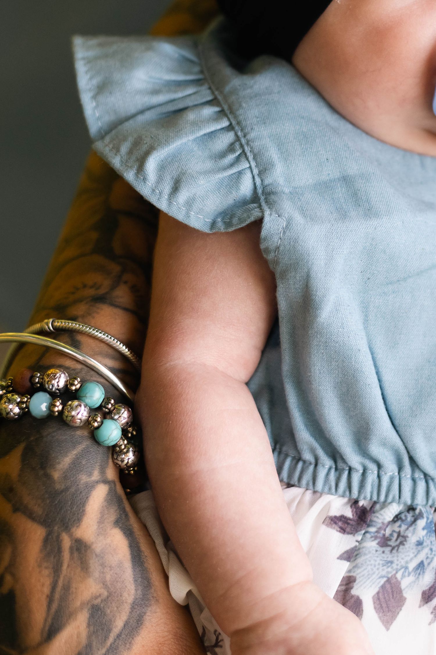 Close-up of tattooed mother's arm adorned with turquoise and gold bracelets holding newborn baby during a newborn session in Boyertown, PA.