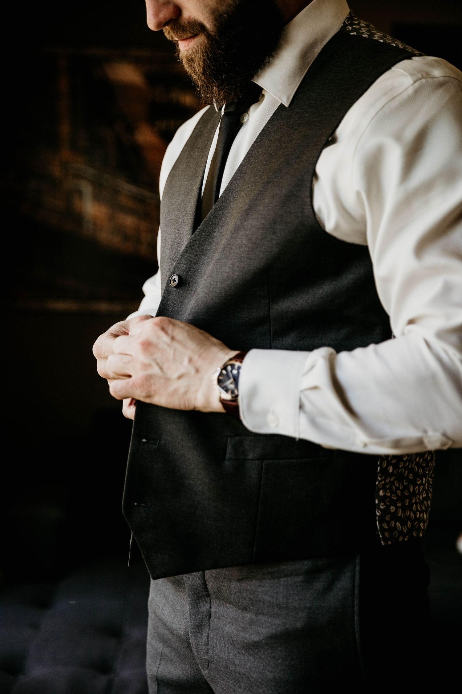 Dapper groom in grey vest and tie adjusts his suit while preparing for his wedding day.