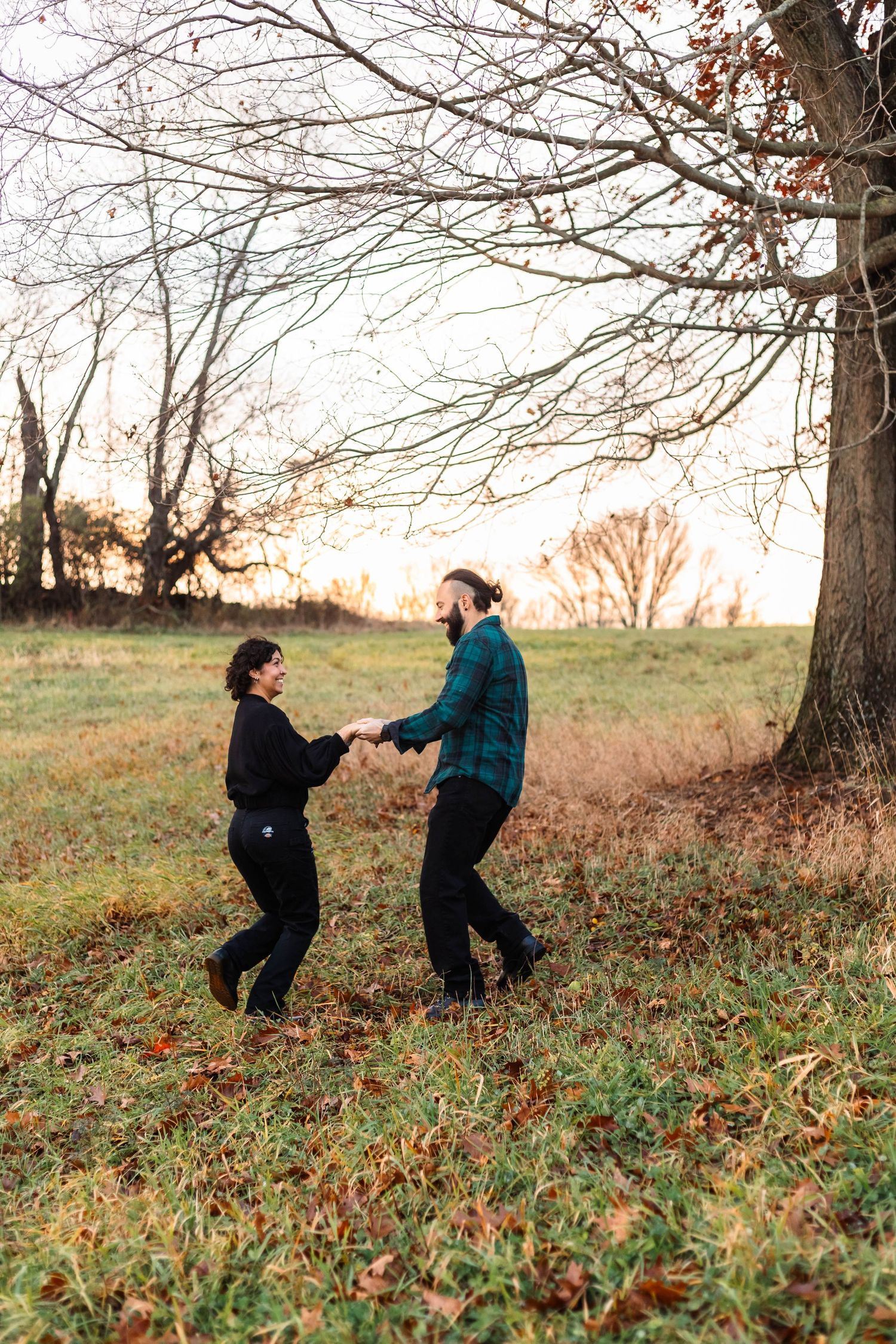 Couple dancing and spinning together in a golden autumn field at sunset near bare trees in West Chester, PA.