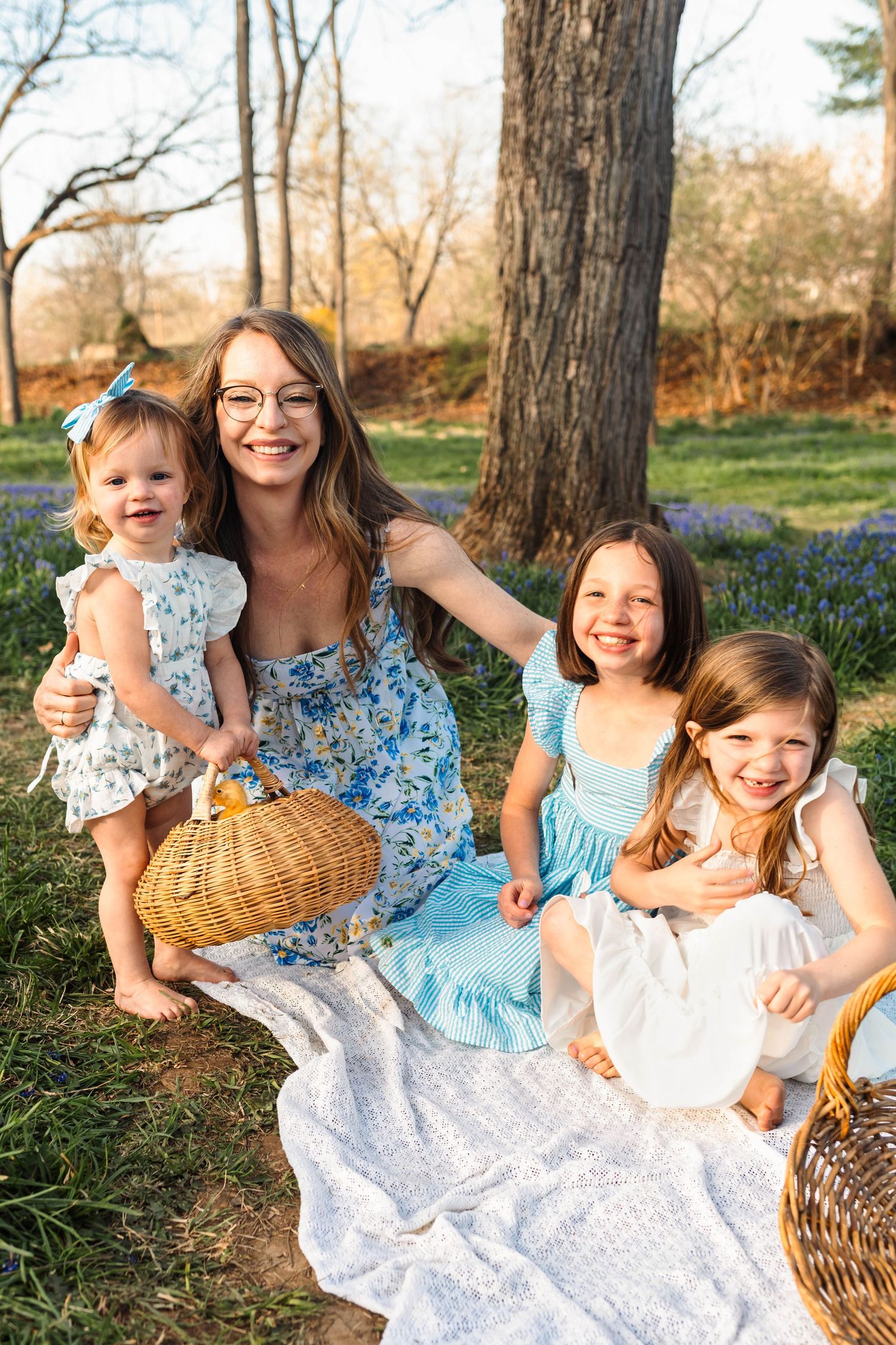 A smiling mother with three young daughters enjoys a spring picnic on a blanket surrounded by blooming bluebells in Alburtis, PA.