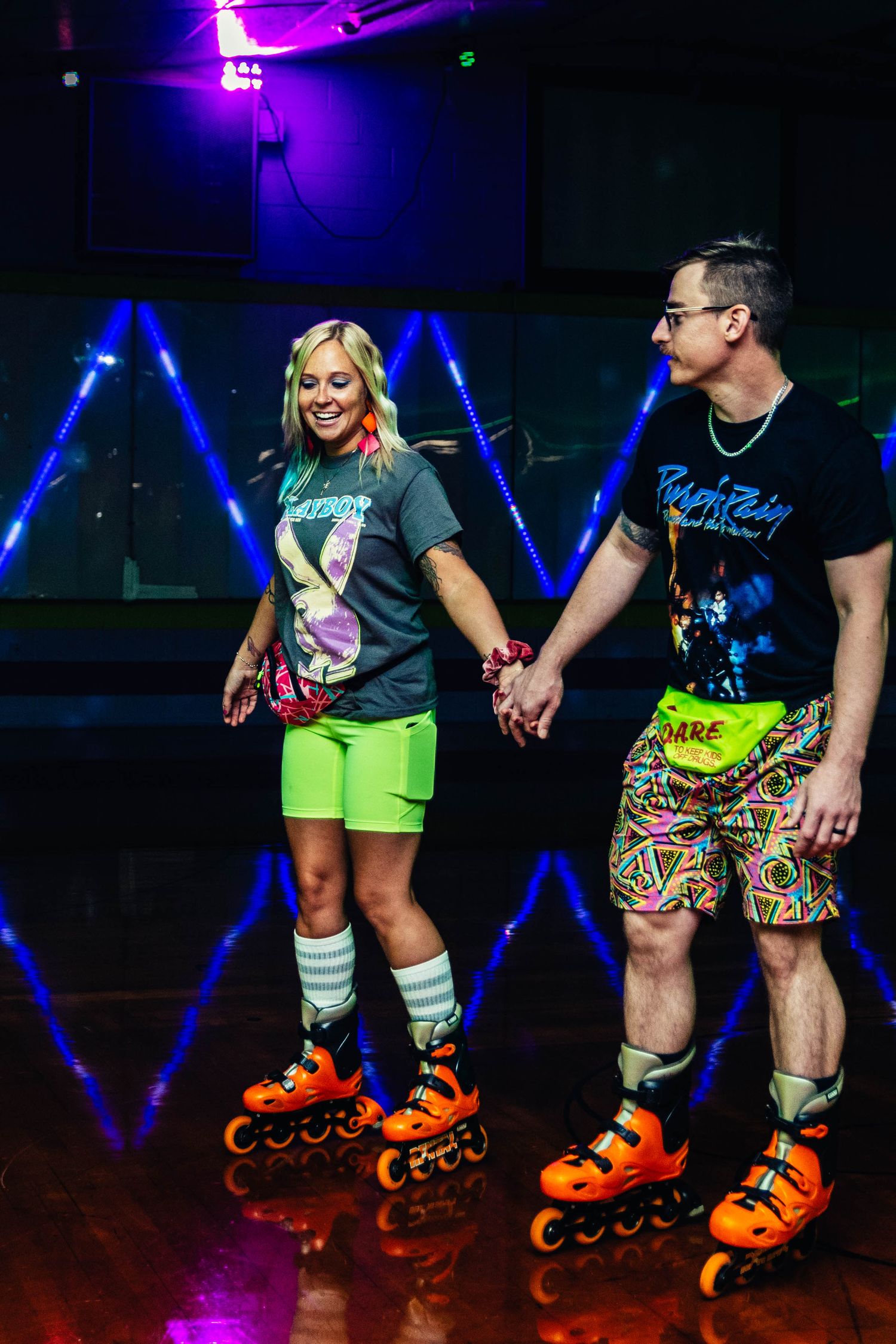 Couple holding hands while roller skating in neon 80s-themed outfits at a colorful skating rink.