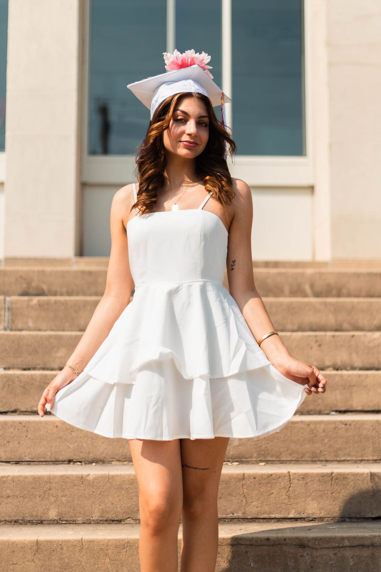 Montgomery County Senior in white ruffled mini dress wearing a white graduation cap with pink tassel on outdoor steps.