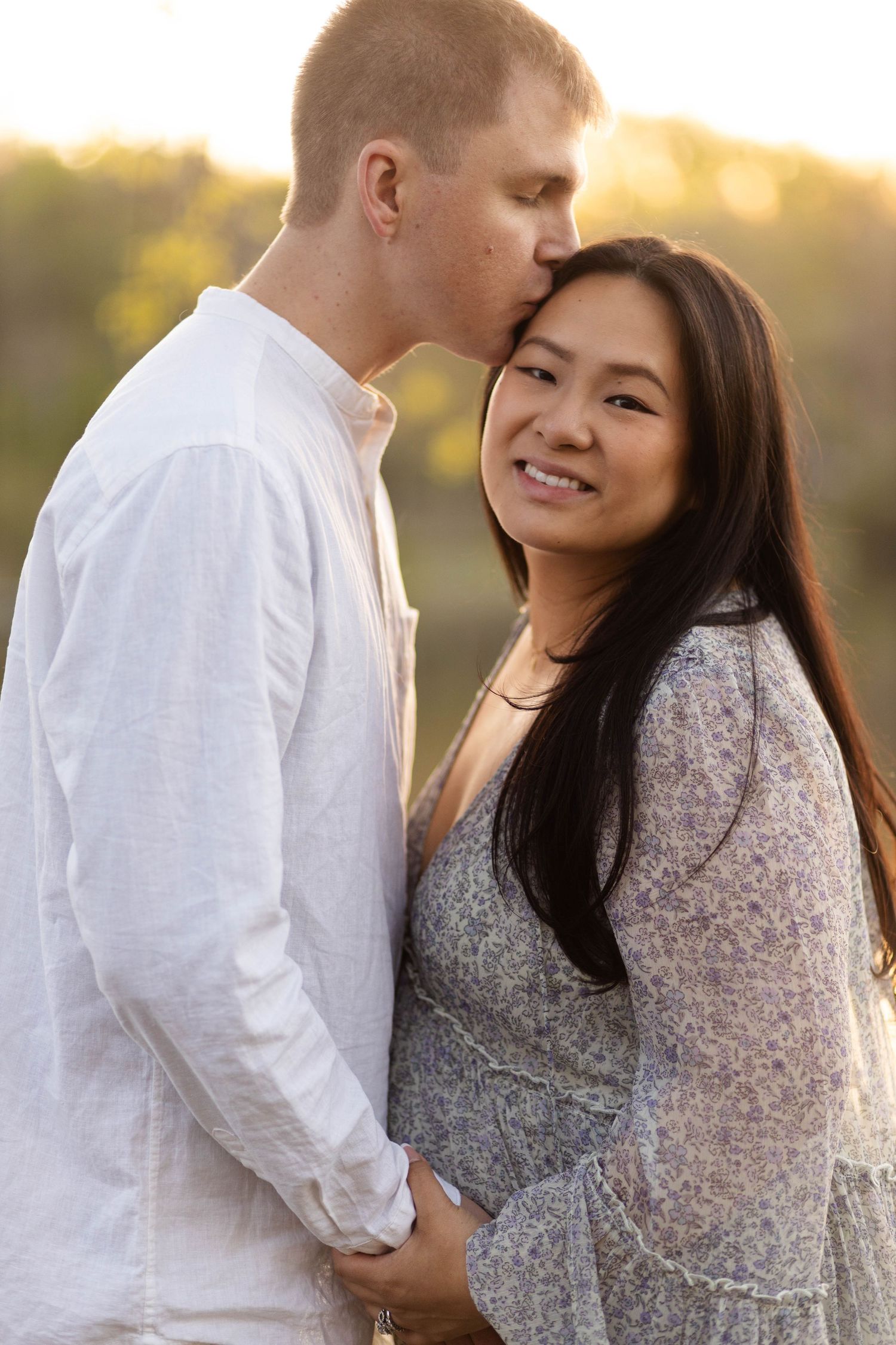 Smiling pregnant woman being kissed on head by partner during golden hour outdoor maternity shoot at Green Lane Park.