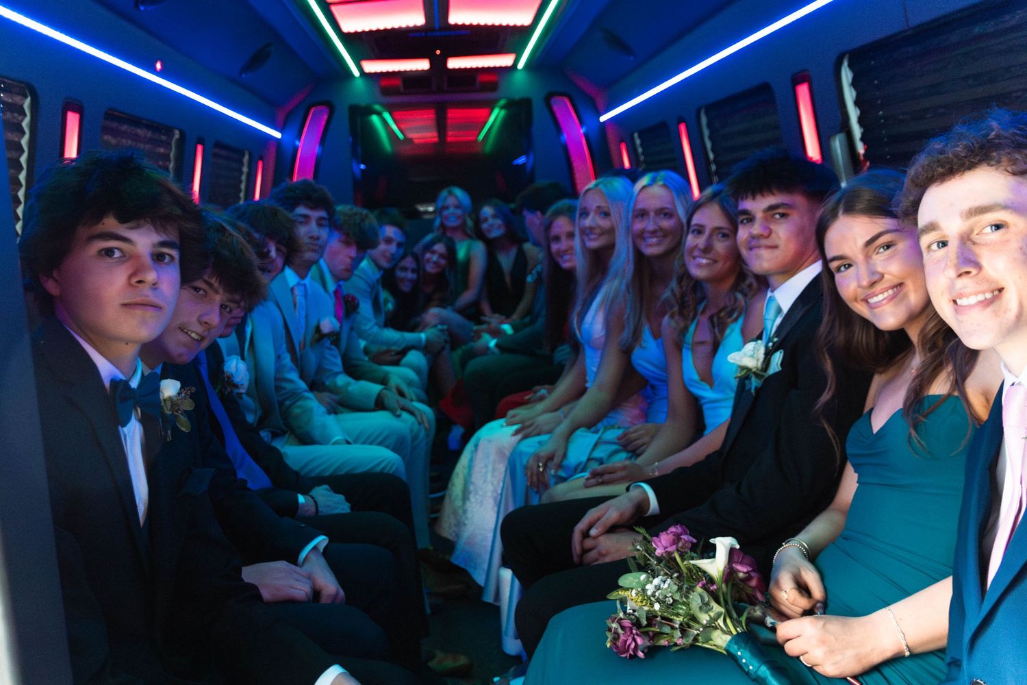 A large group of Perkiomen Valley High School students in formal prom attire smile together inside a decorated party bus.