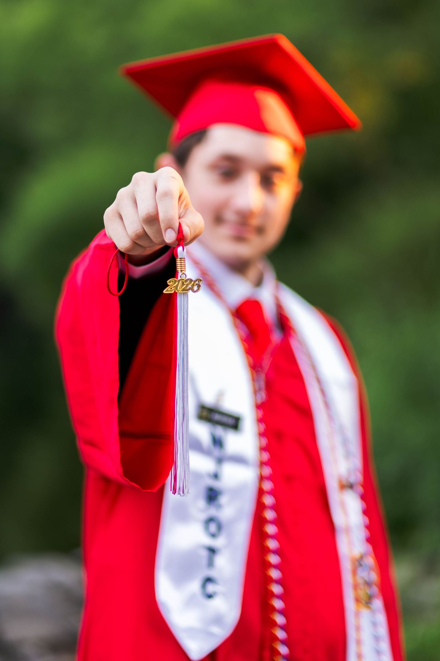 Owen J Roberts High School graduate in red cap and gown holding tassel with 2025 charm toward camera.