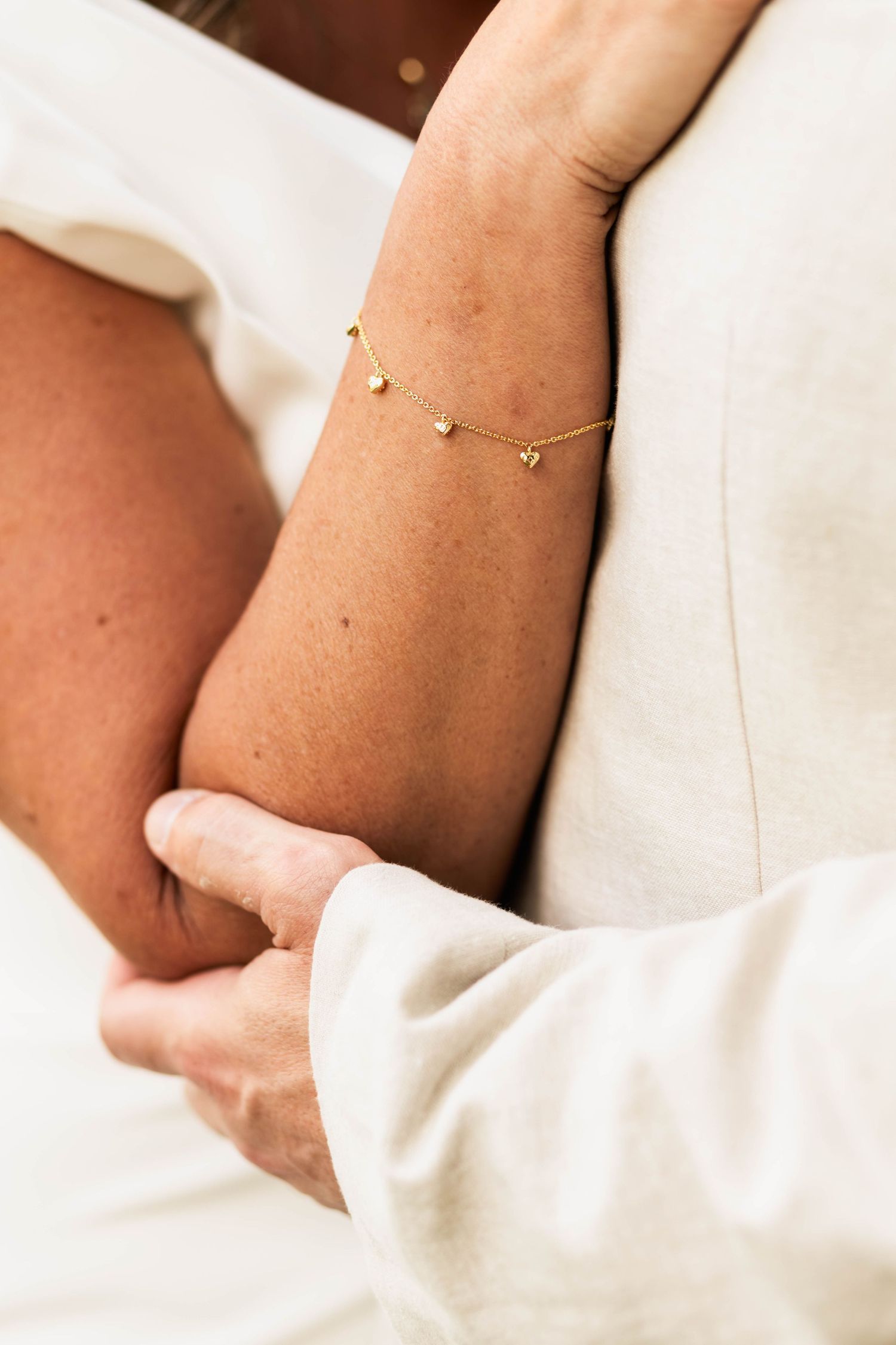 Close-up of bride wearing delicate gold chain bracelet with small charms on her wedding day.