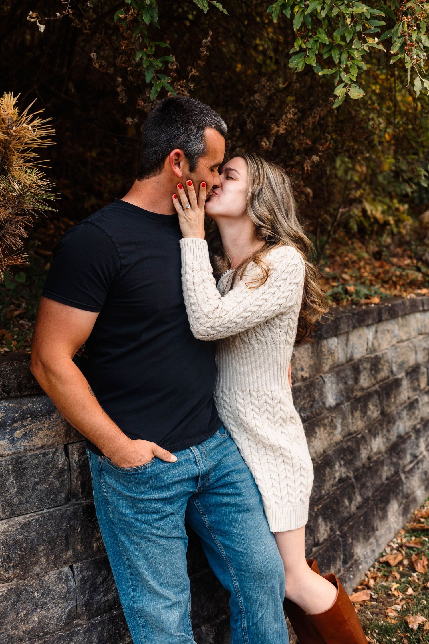 Couple sharing a romantic kiss against a stone wall surrounded by lush green foliage in Boyertown, PA.