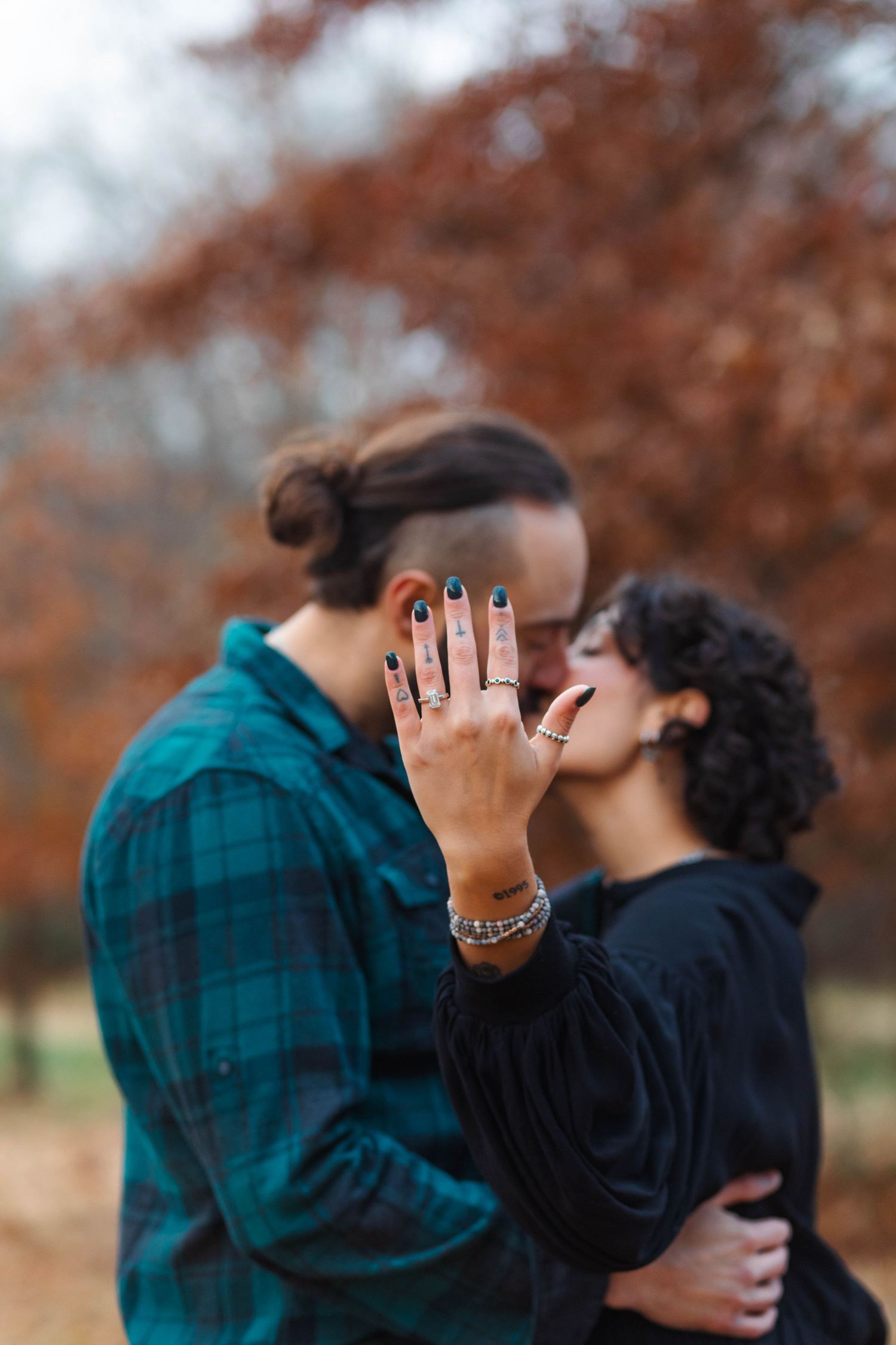 Engaged woman showing off rings while kissing partner in front of red autumn foliage in West Chester, PA.