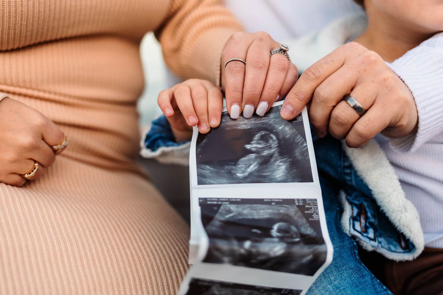 Couple holding ultrasound photos together showing wedding rings on their hands at Green Lane Park in Green Lane, PA.