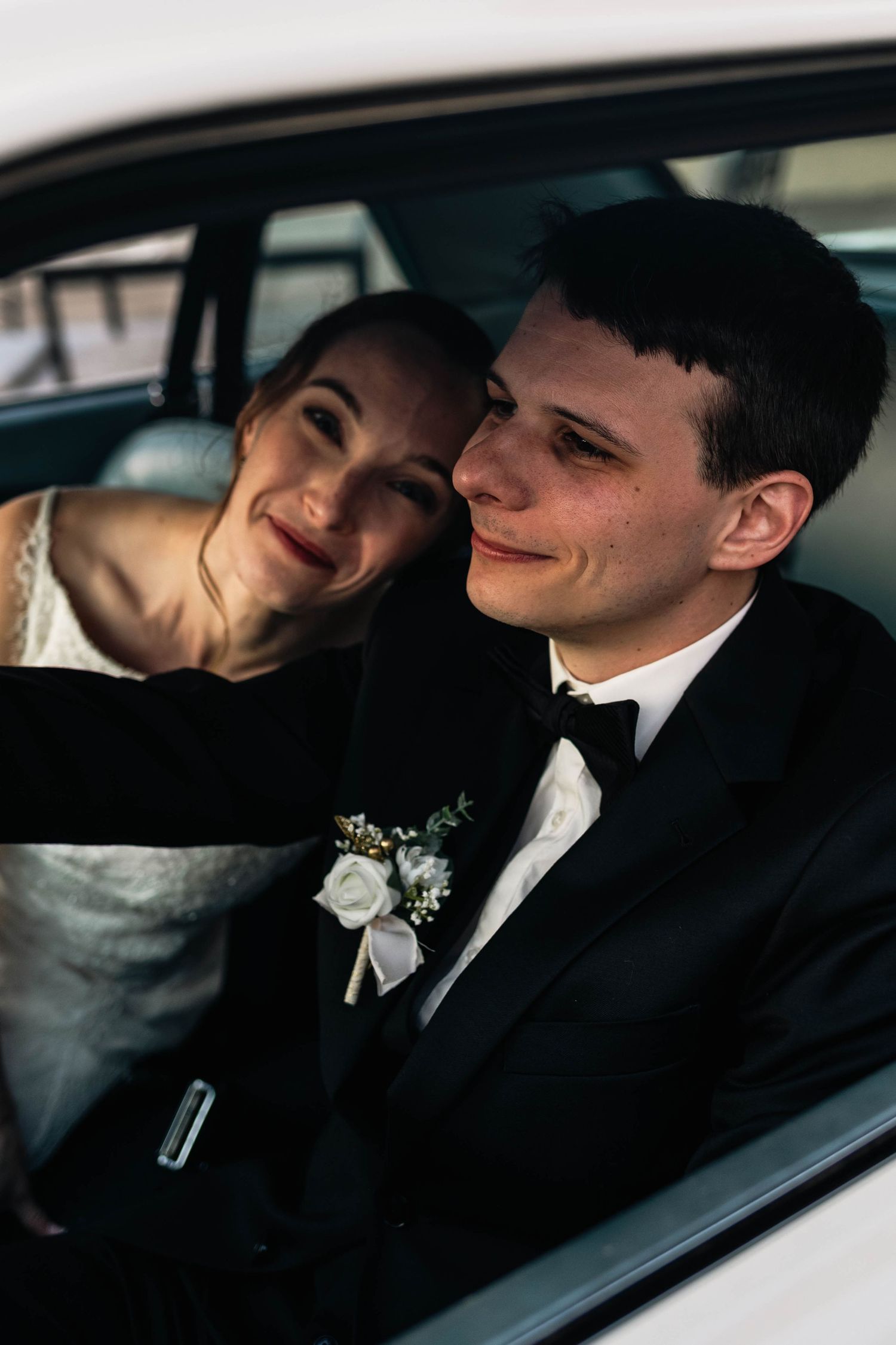 Newlywed bride resting her head on grooms shoulder while sitting together in a classic car.