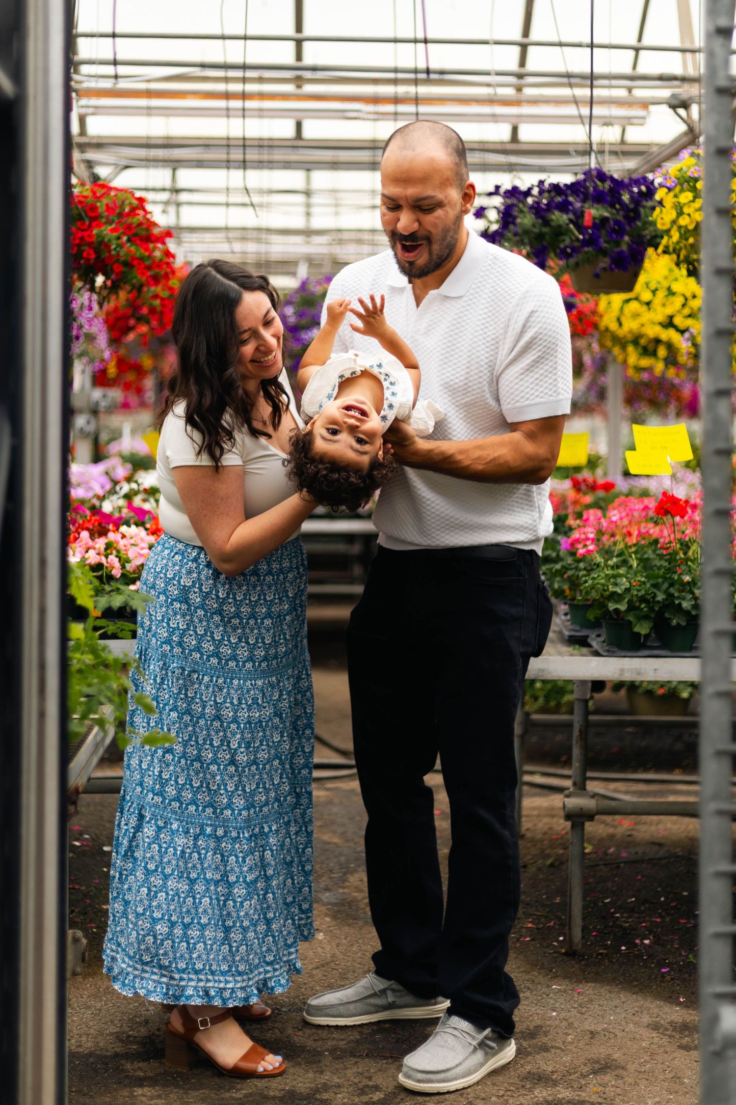 A joyful family with a baby laughs together inside a colorful flower greenhouse.