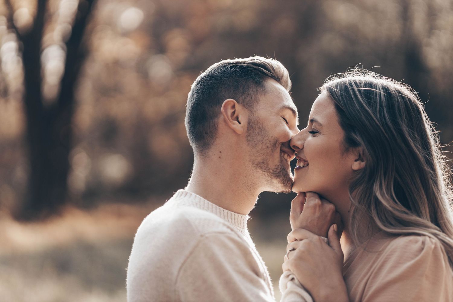 Happy couple sharing a romantic almost-kiss moment outdoors in autumn forest setting.