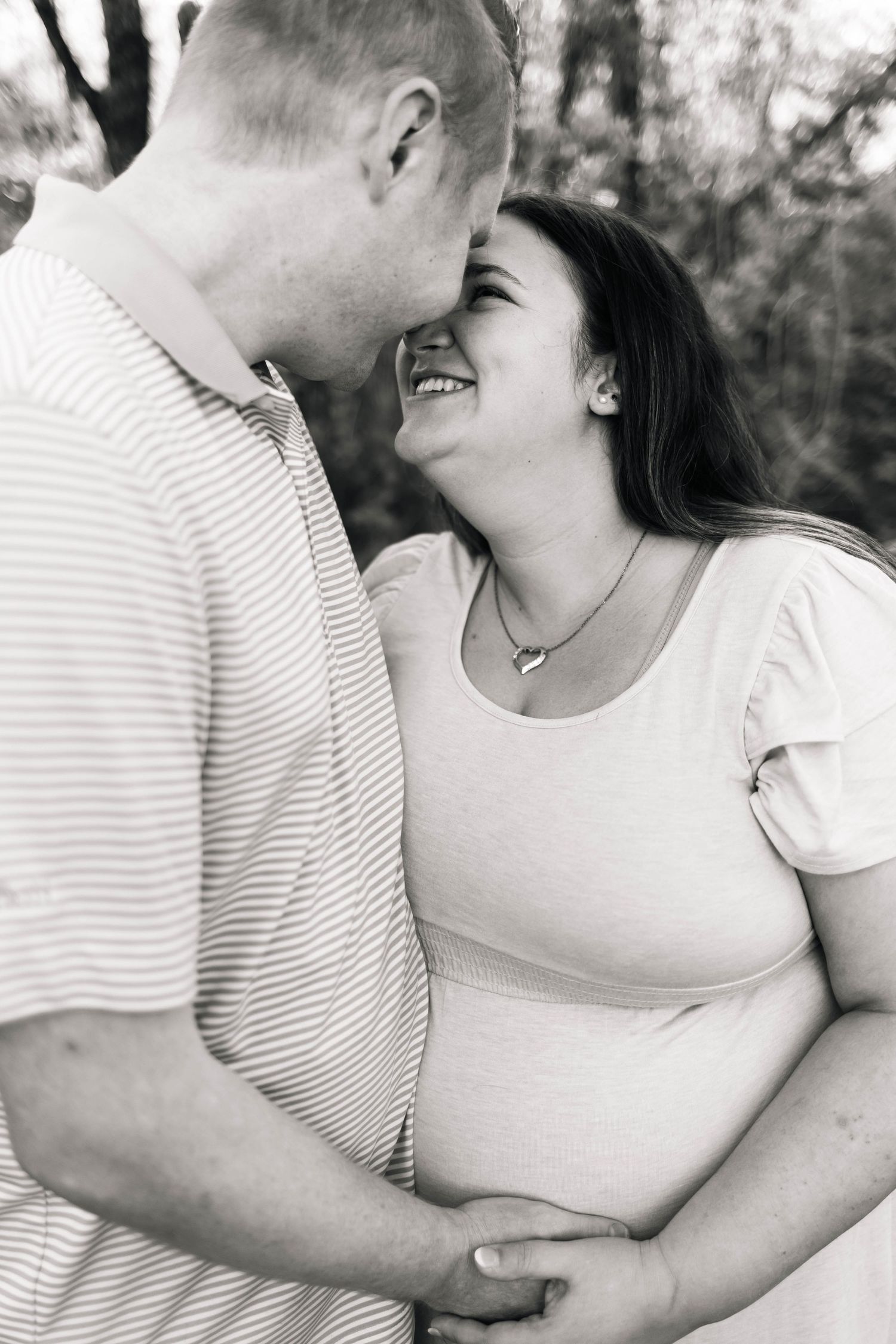 Black and white photo of a smiling pregnant woman and her partner sharing a tender moment outdoors in Philadelphia, PA.