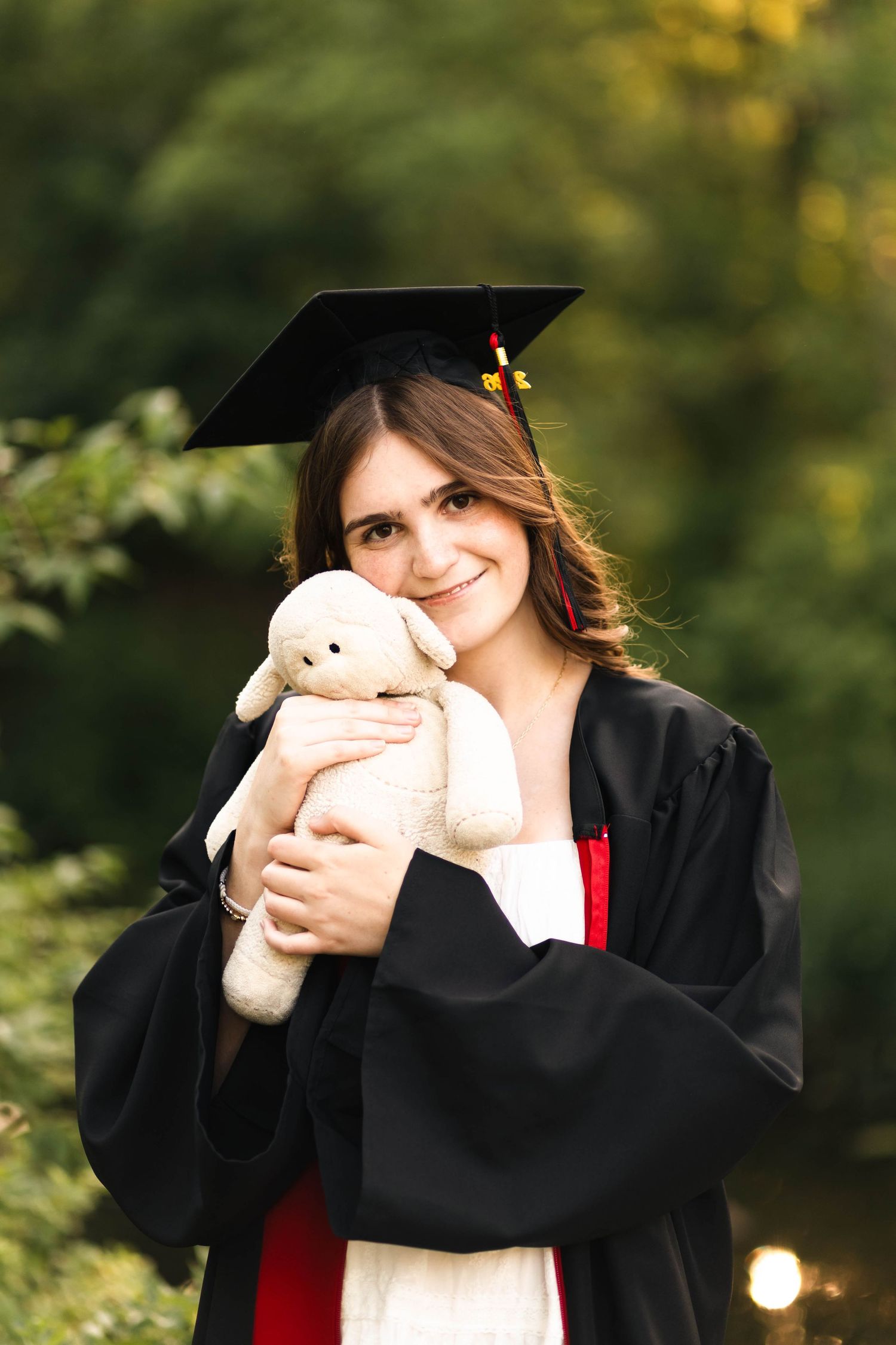 Boyertown Senior in graduation cap and gown hugging a stuffed teddy bear, smiling outdoors.