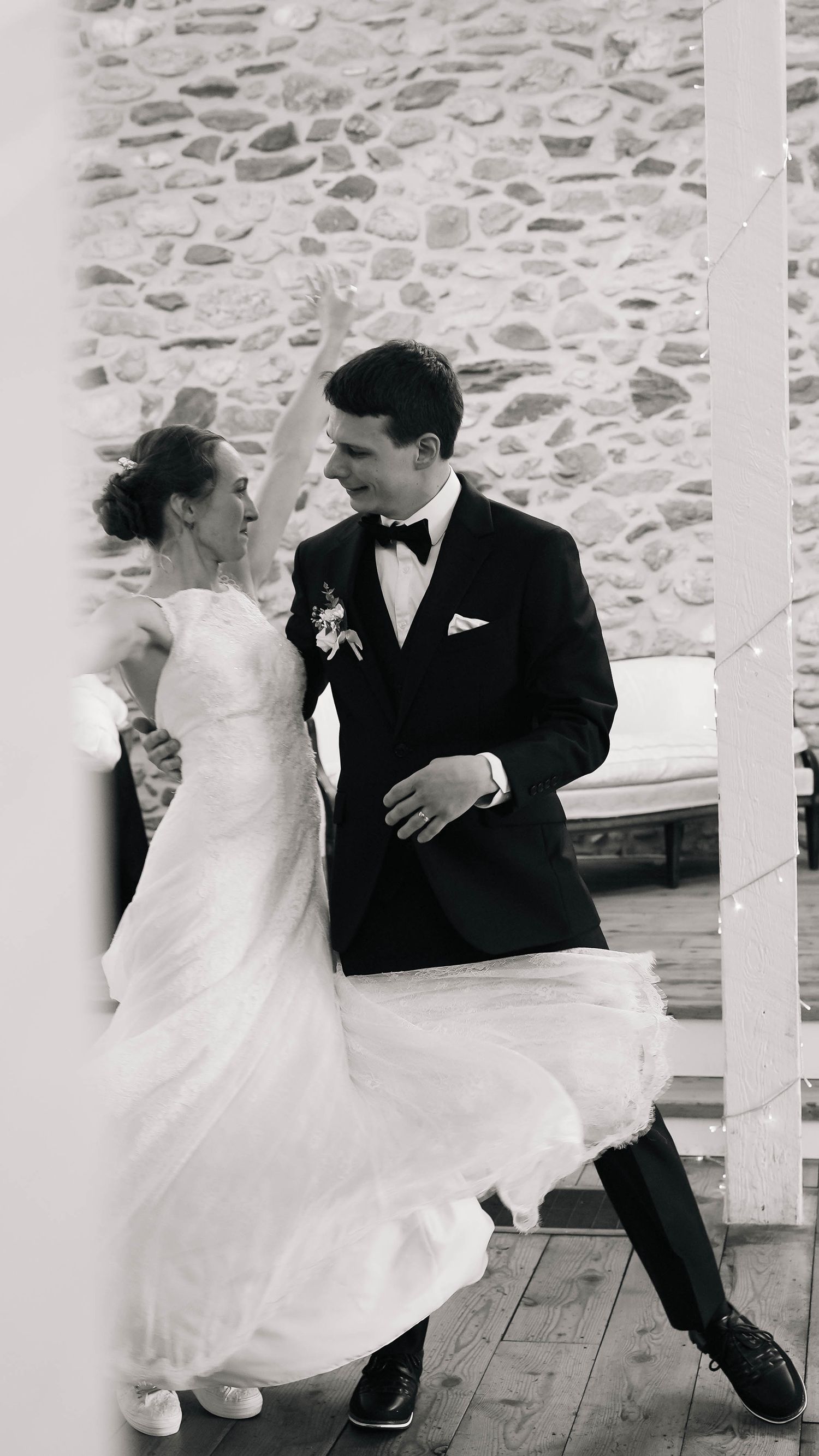 Black and white photo of joyful bride and groom dancing together at their wedding reception.