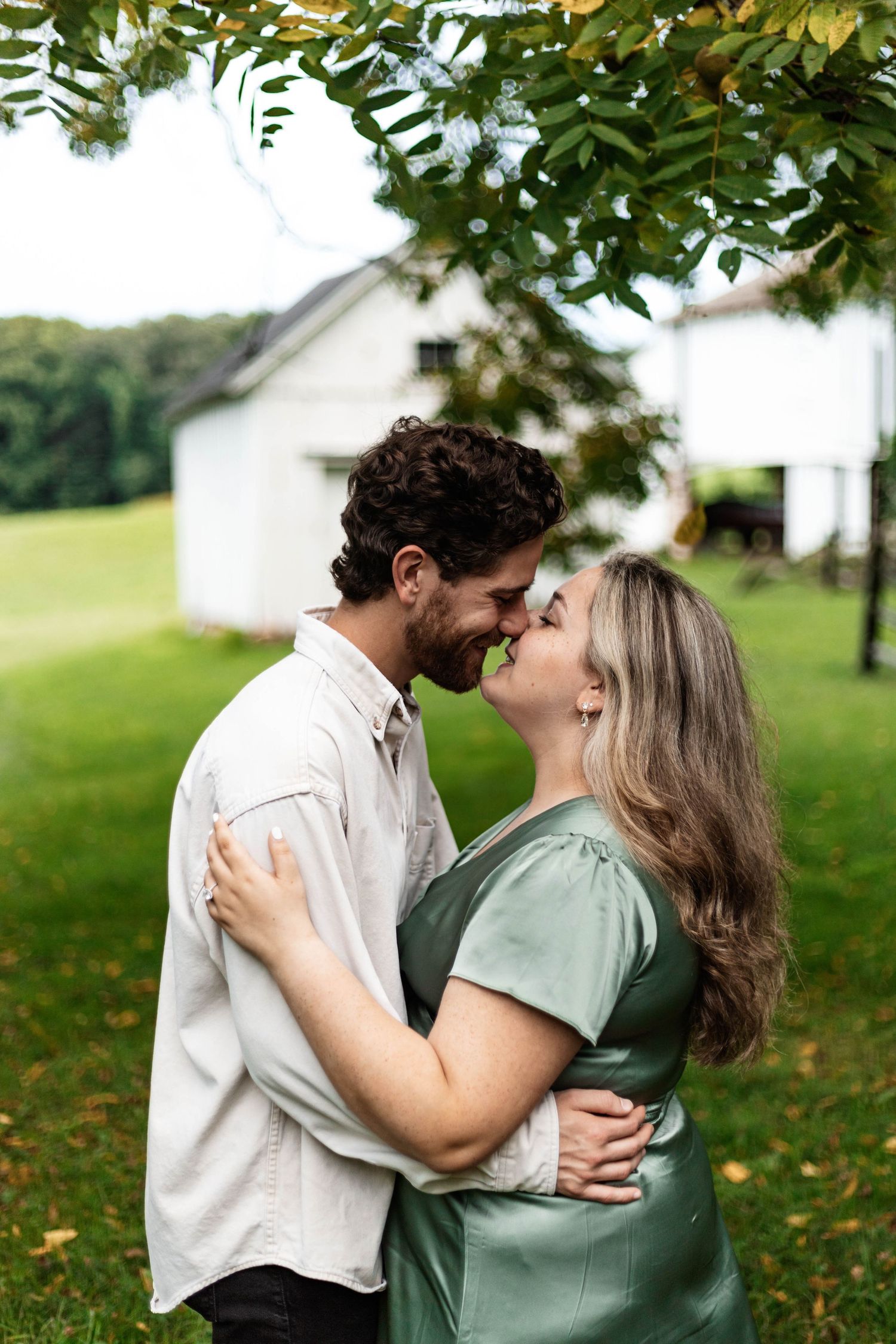 Happy couple sharing a romantic almost-kiss while embracing outdoors near a white farmhouse.