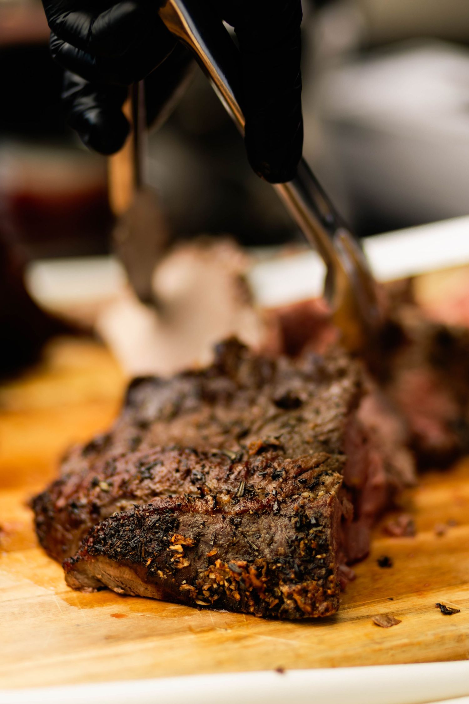 Chef in black gloves slicing a perfectly seared steak on a wooden cutting board at a wedding reception.