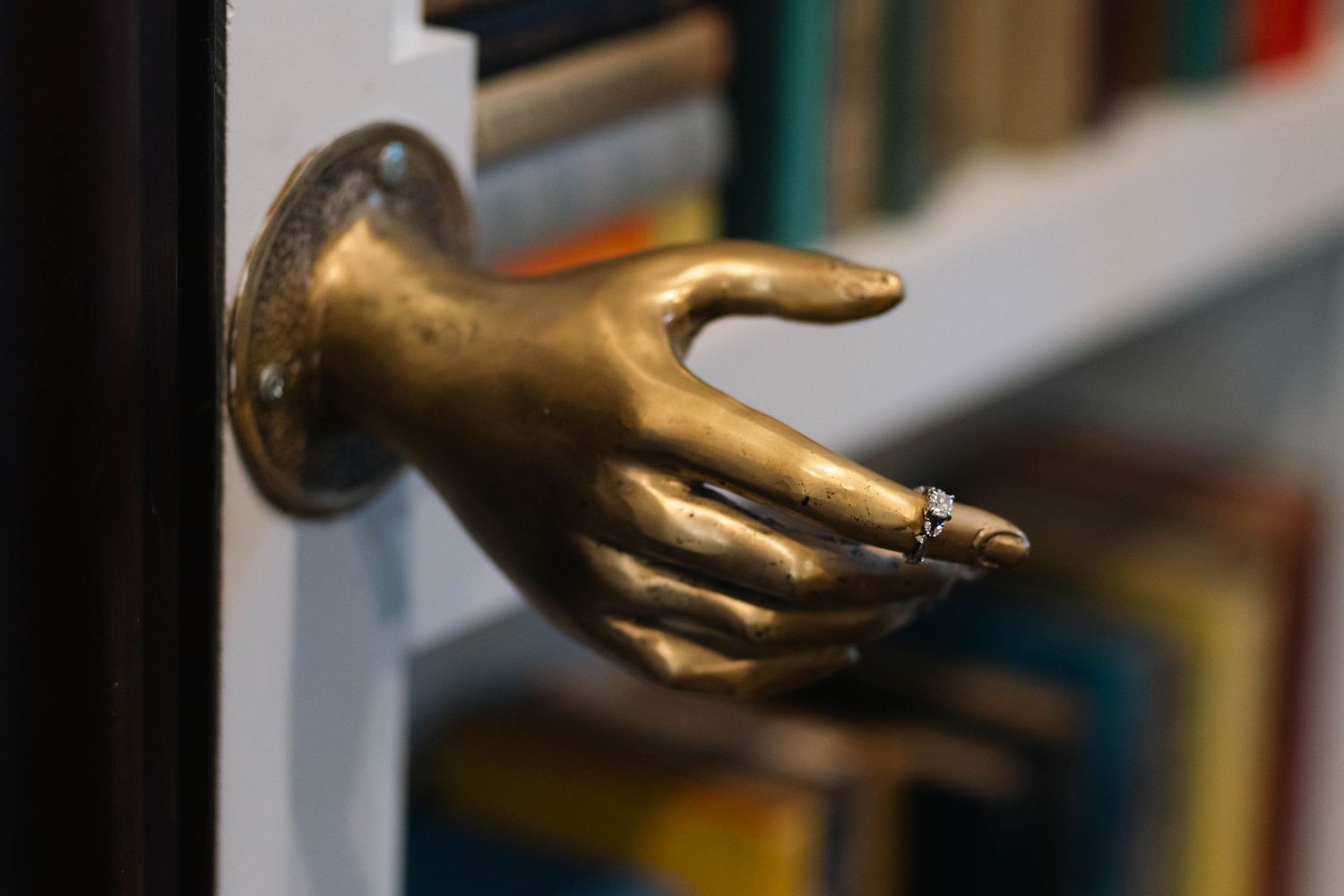 Ornate gold hand-shaped door knocker mounted on a dark wooden door beside a bookshelf in West Chester, PA.
