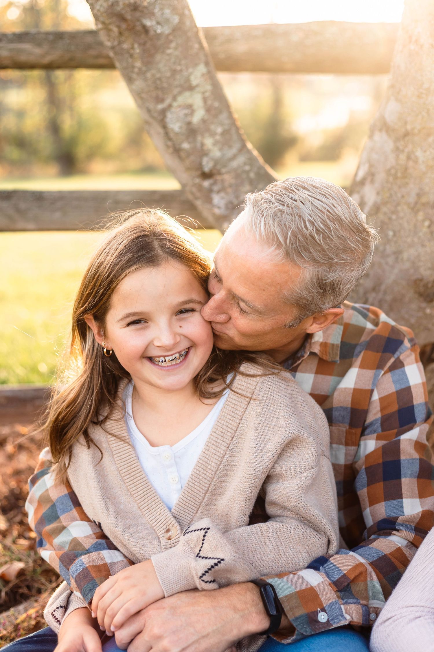A father kisses his laughing daughter on the cheek while sitting outdoors in warm sunlight in Harleysville, PA.