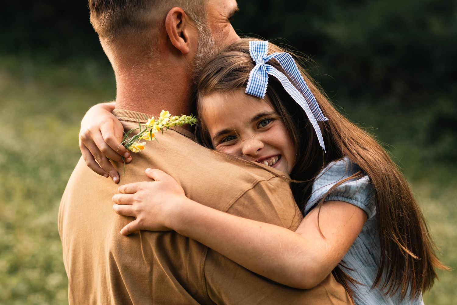 Young girl with blue bow hugging her father tightly while smiling outdoors in nature in Boyertown, PA.