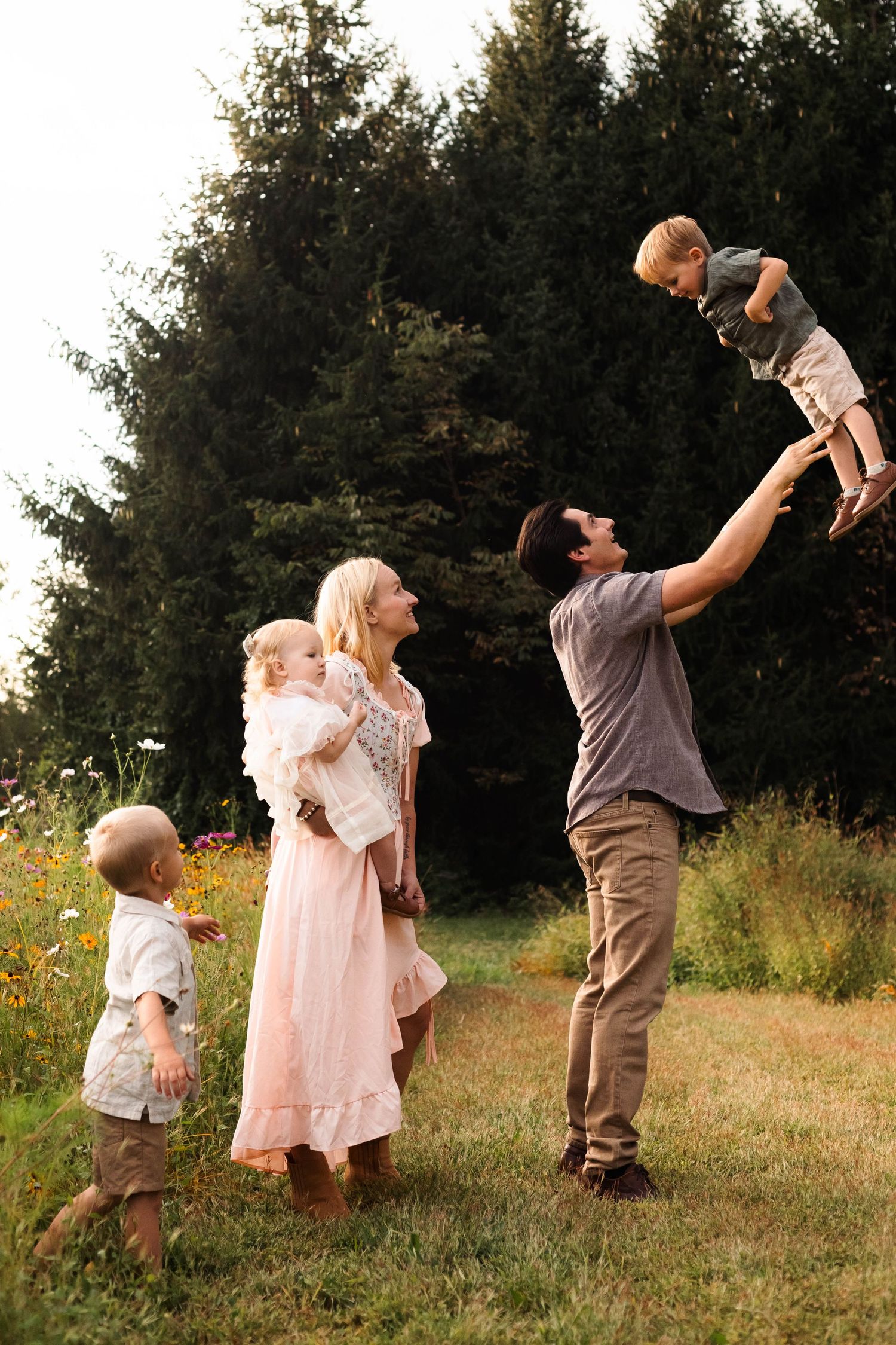 Family of five enjoying outdoor time with father lifting son in the air near evergreen trees in Pekriomenville, PA.
