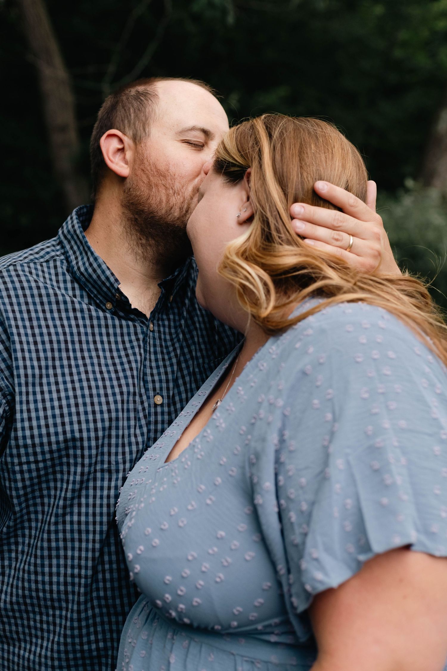 Bearded man tenderly kisses woman in blue dress on forehead in romantic outdoor couples portrait in Boyertown, PA.