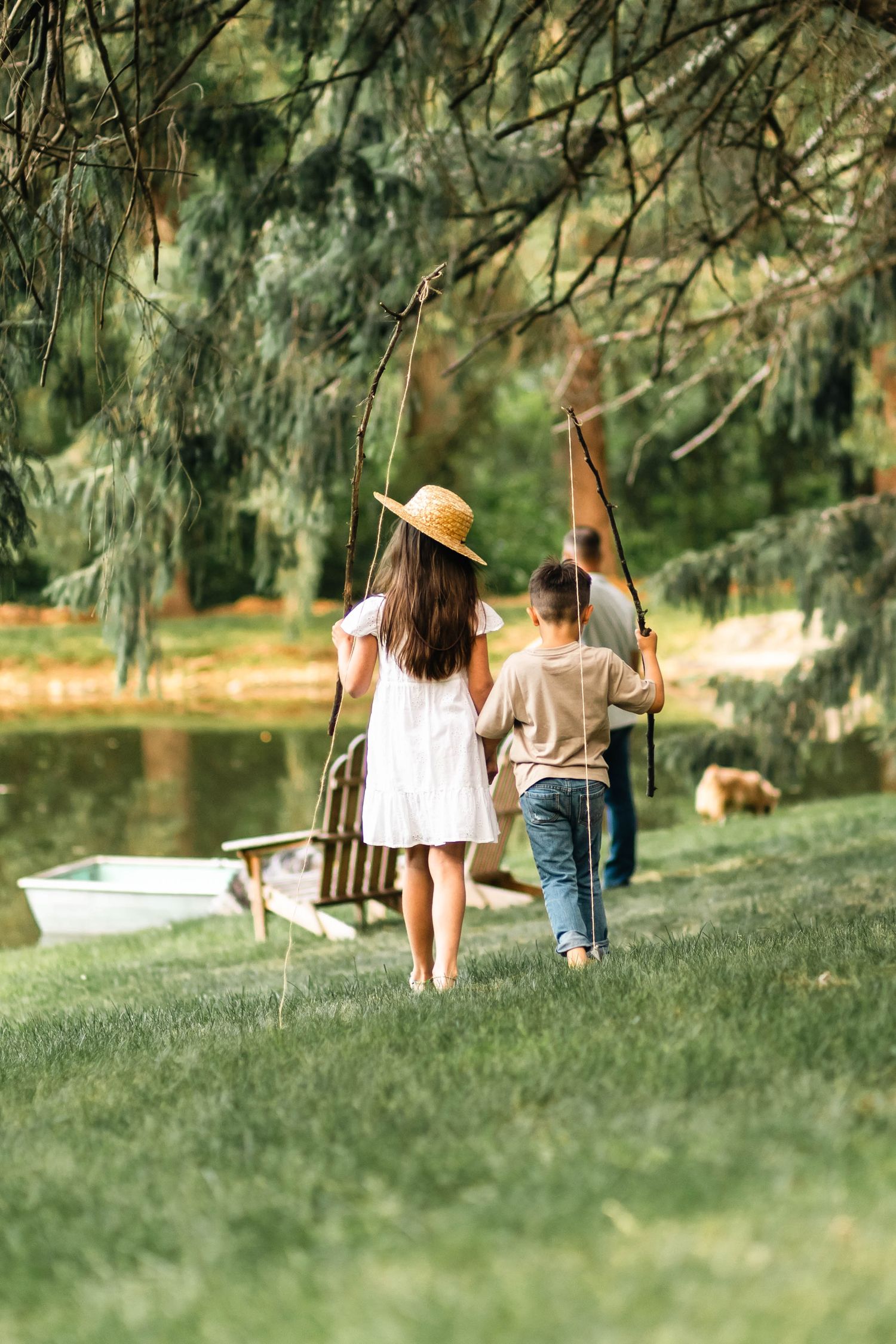 Two children walking hand-in-hand toward a wooden swing near a peaceful pond under trees in Boyertown, PA.