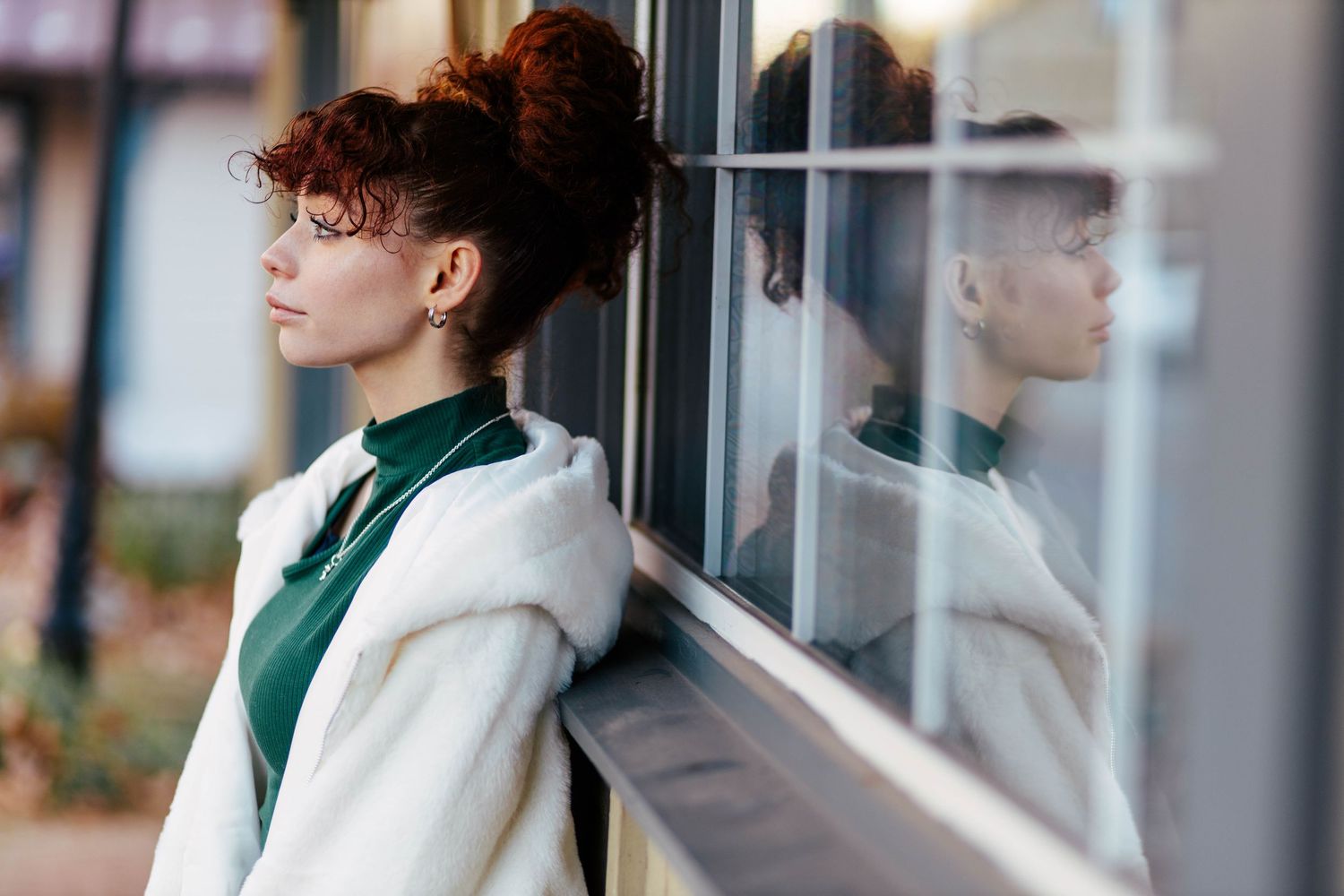 Pottstown Senior session with the senior in white fur coat leaning against a window with her reflection visible in the glass.
