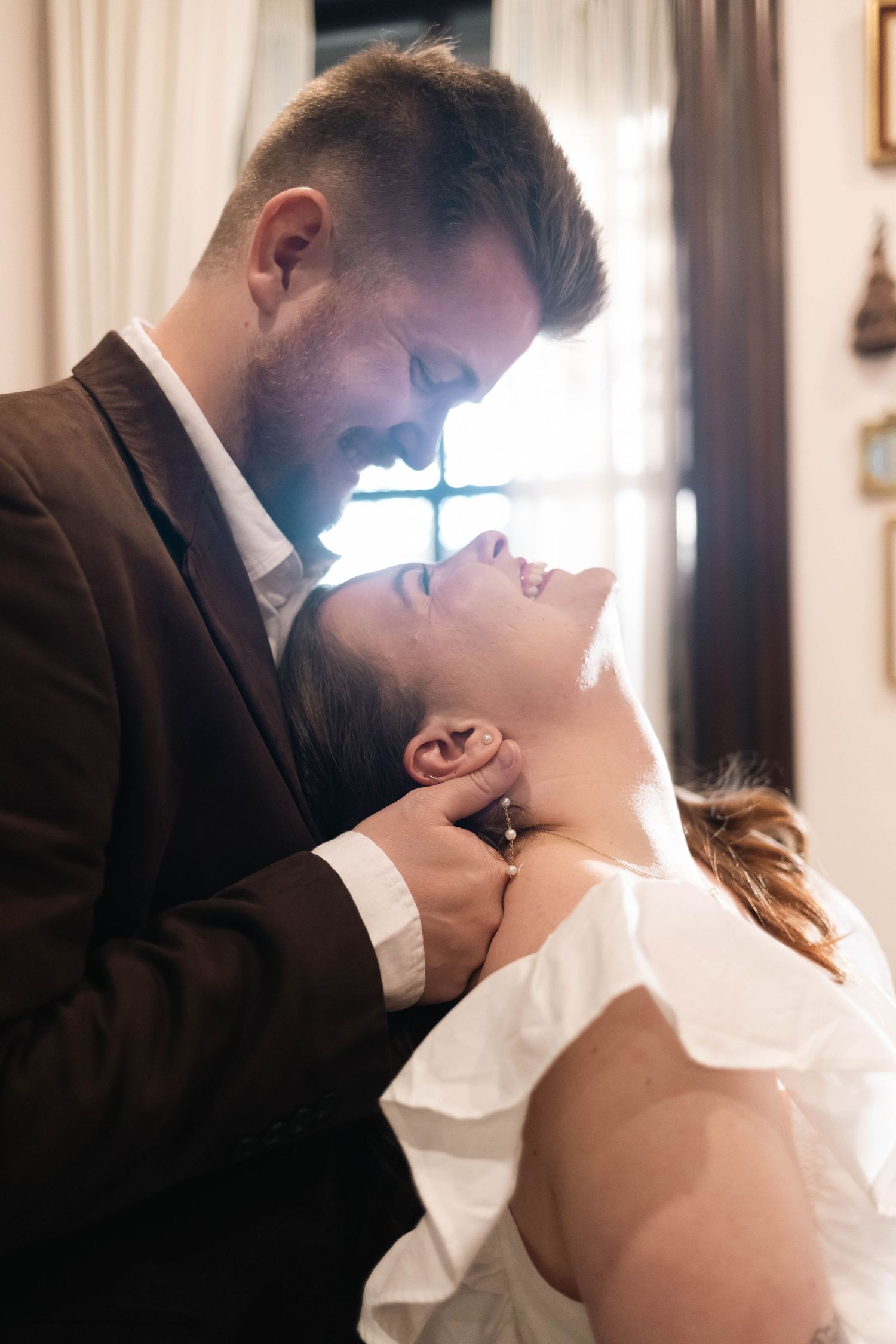 Romantic couple sharing an intimate moment, man tenderly holding woman's face near a window in West Chester, PA.
